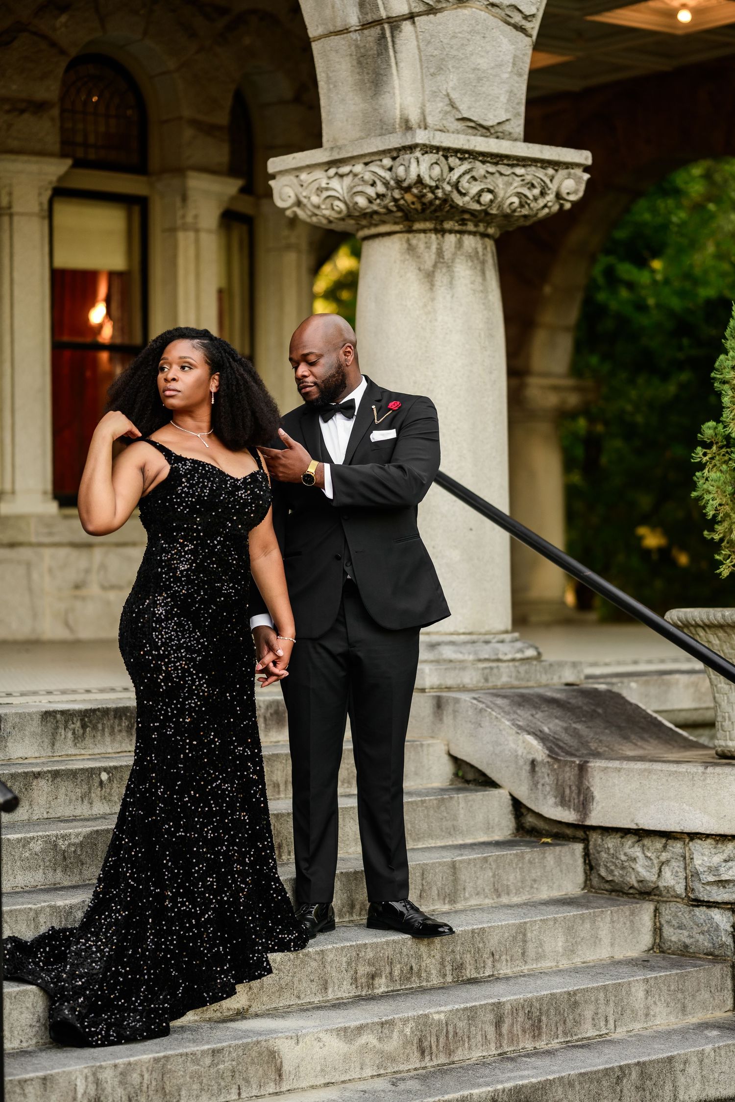 Couple in black formal wear share intimate moments on historic stone staircase.