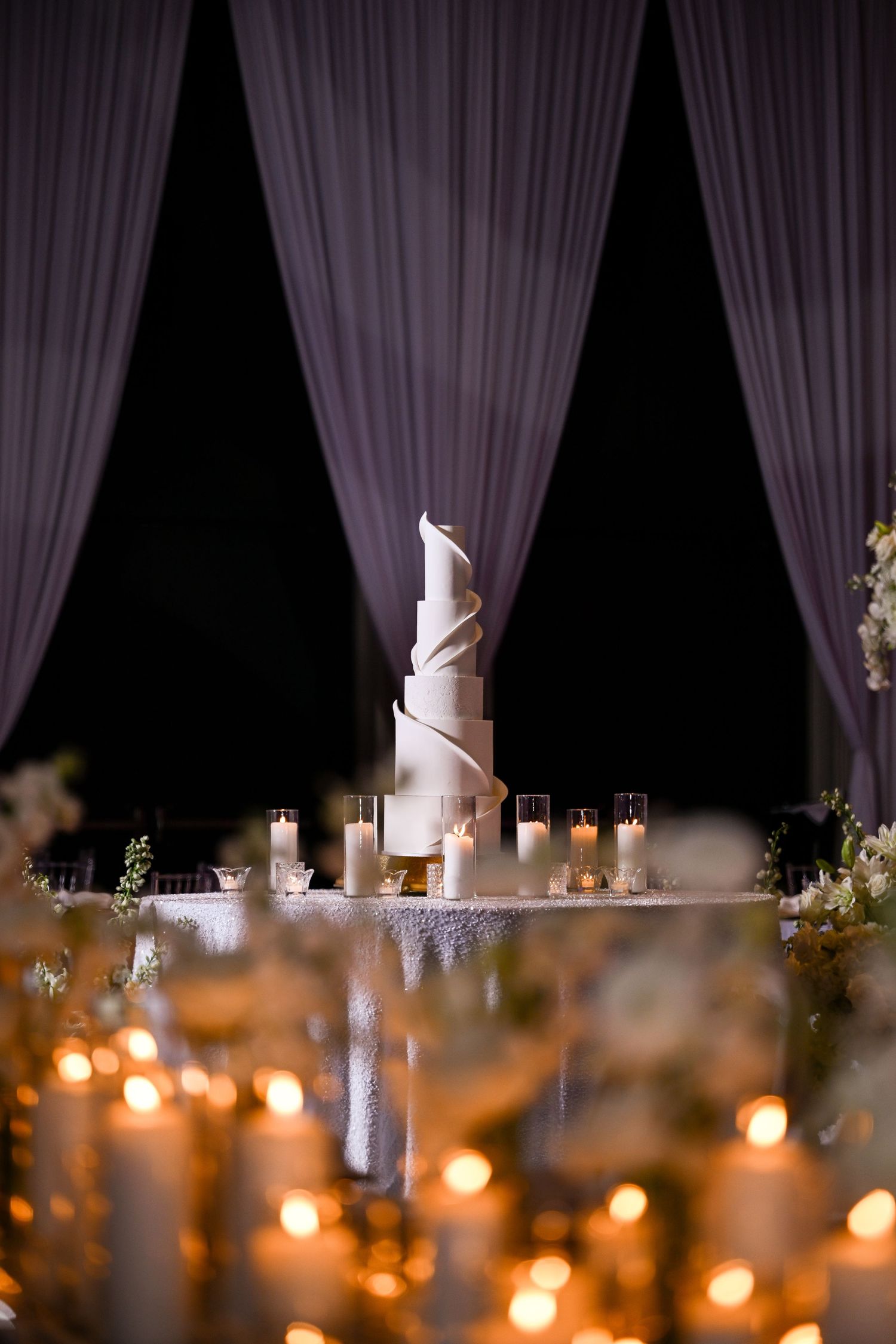Dramatic wedding cake display with candlelight and purple draping creating an ethereal atmosphere.