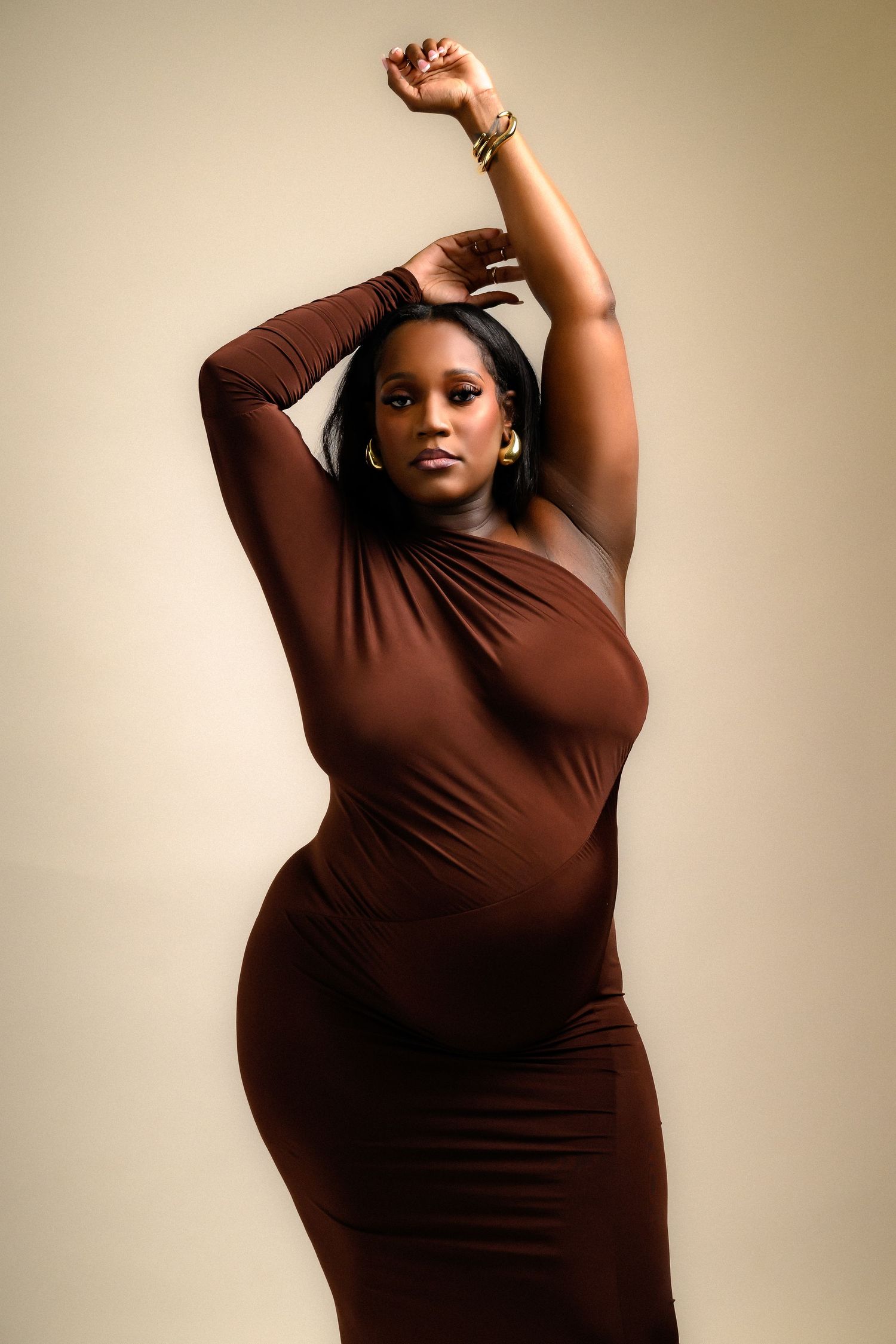 Solo maternity poses in brown dress against neutral background showing pregnancy silhouette.