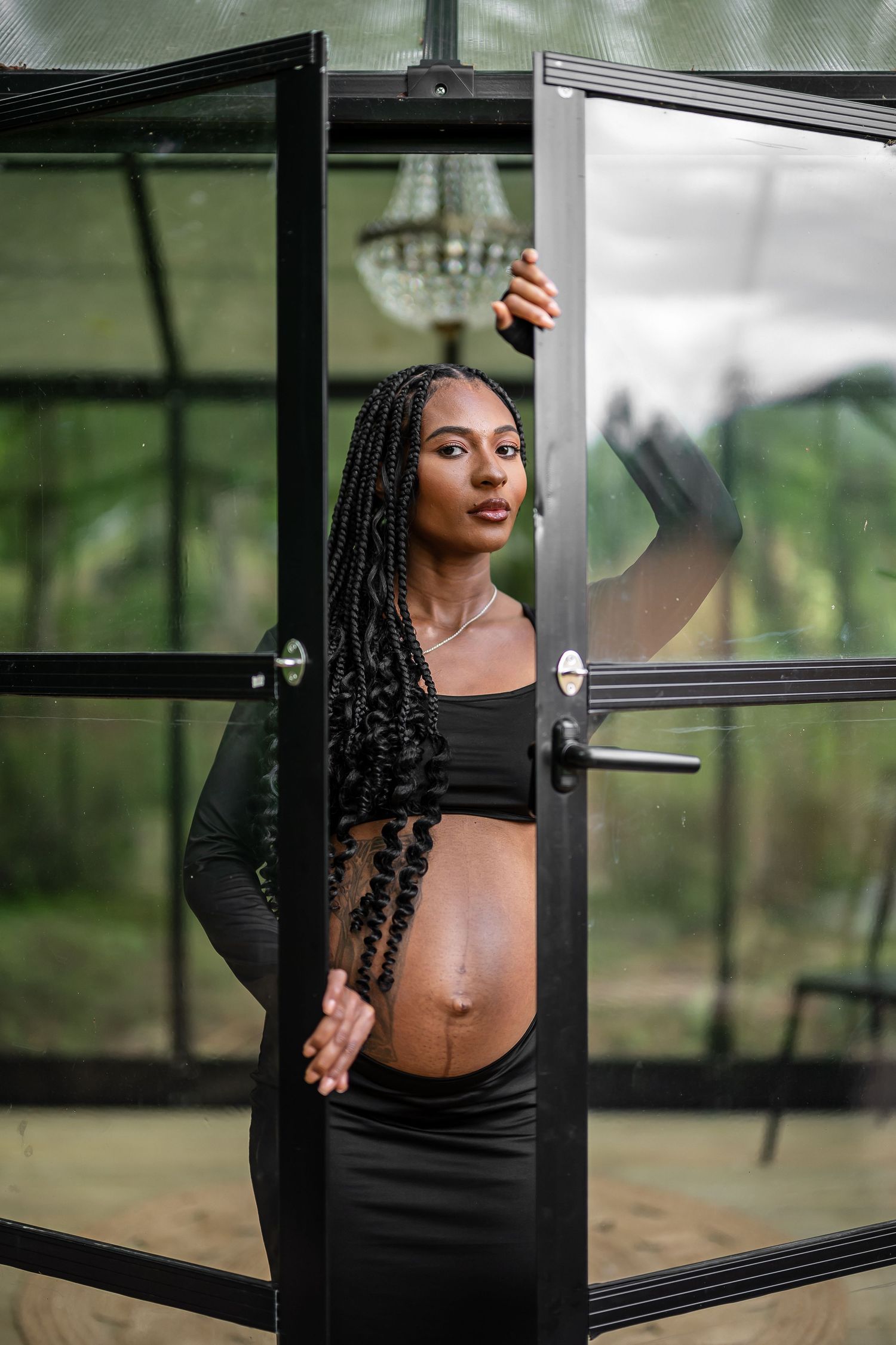 Artistic portrait session in a greenhouse featuring black clothing against glass and metal architecture.
