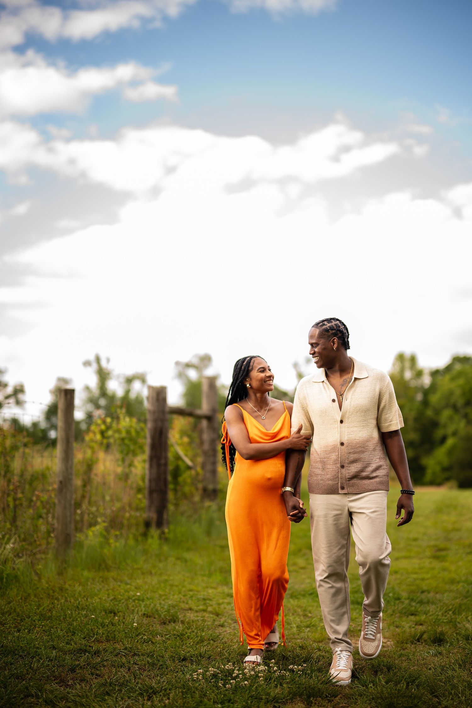 A couple walks together through a grassy field on a bright, cloudy day.
