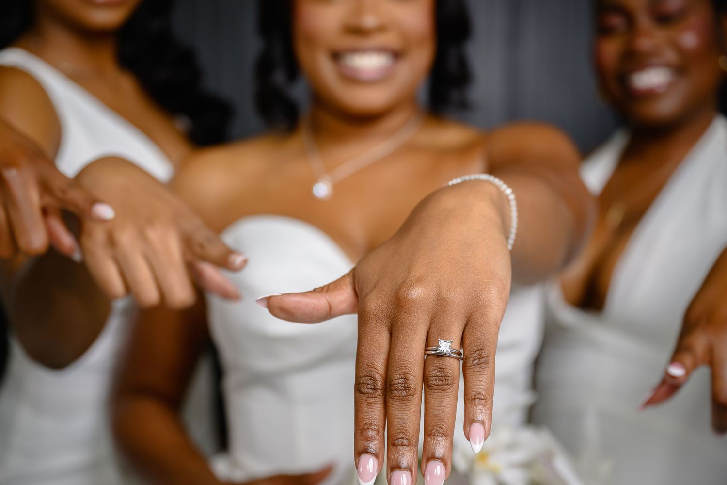 Close up photo of hands with white manicured nails showing off engagement rings.