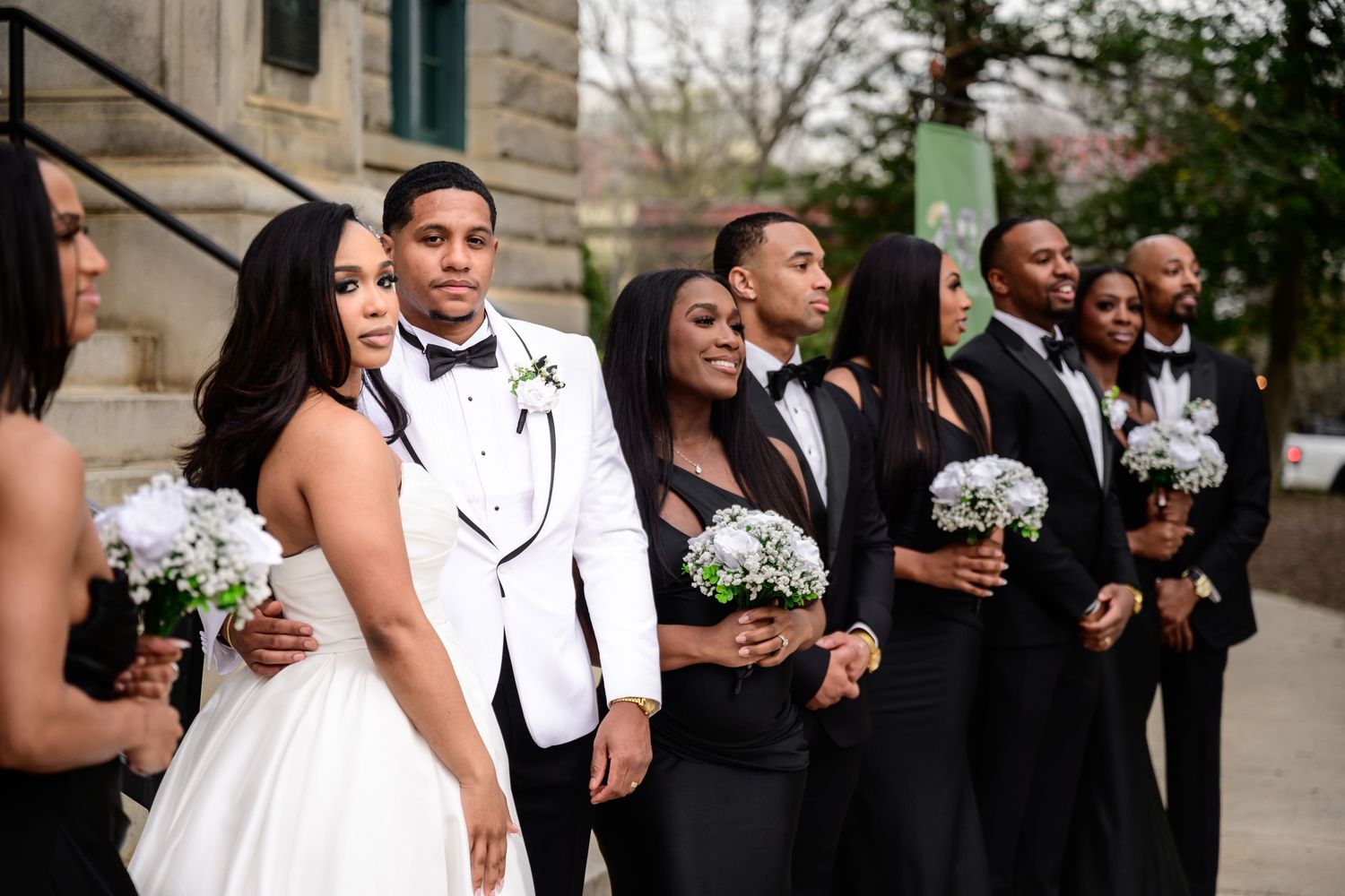 Wedding party lined up against stone building exterior in formal attire.