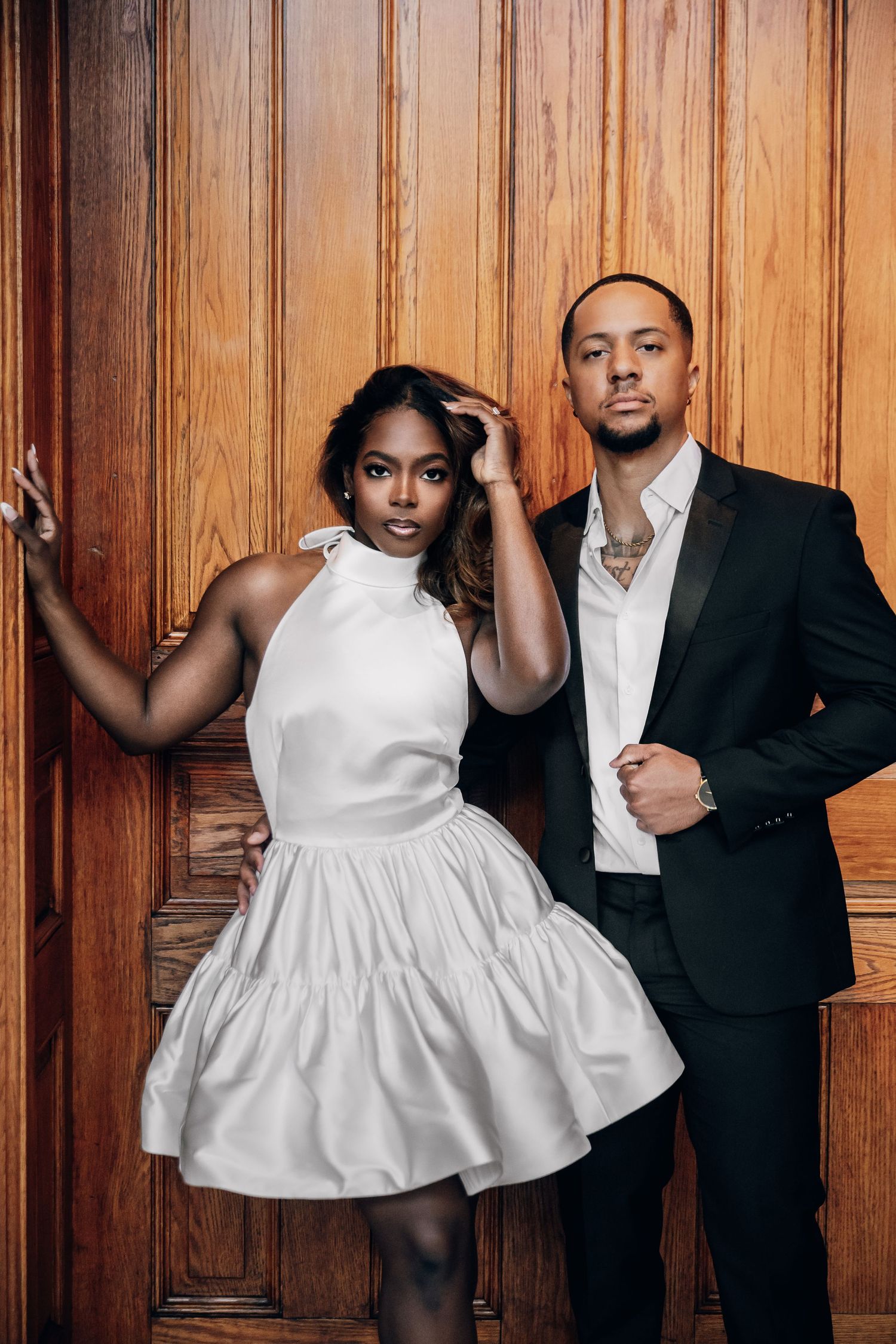 Stylish couple poses against wooden paneling in contrasting black and white formal attire.