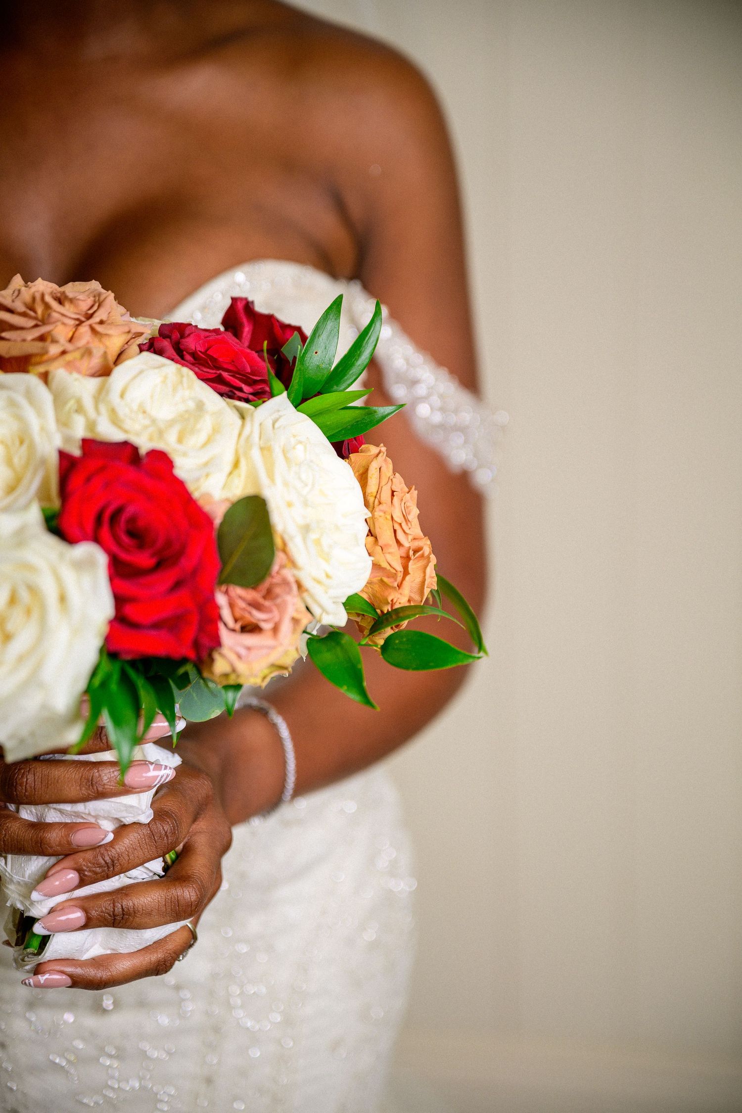 Bridal bouquet featuring cream and red roses with lush green foliage.