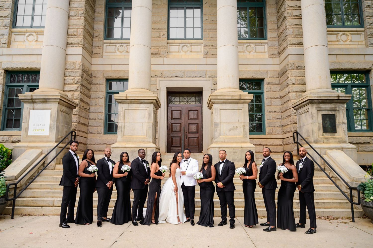 Panoramic shot of wedding party arranged on stone steps of classical building.