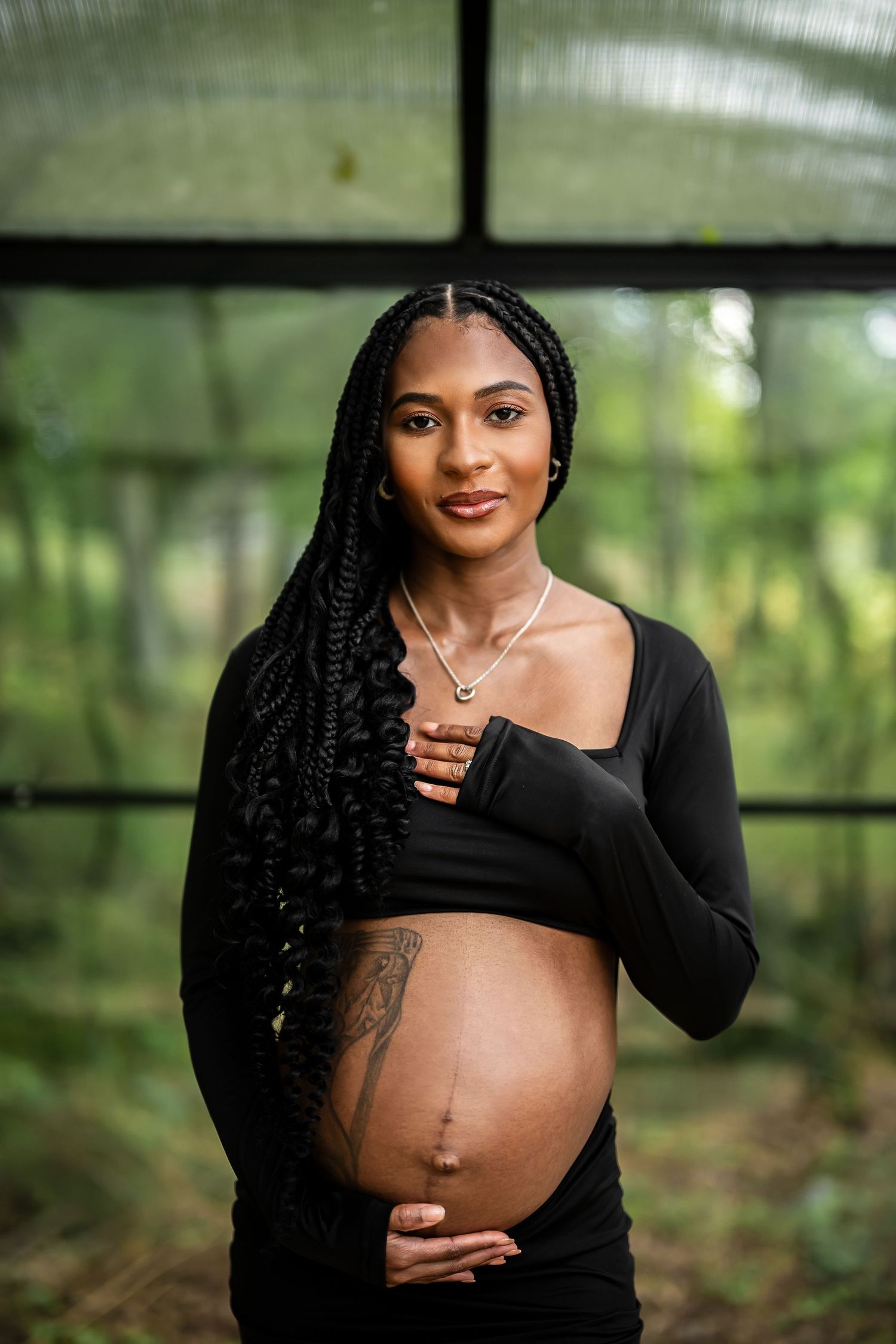 A maternity portrait session showcases an elegant black dress against a greenhouse backdrop.
