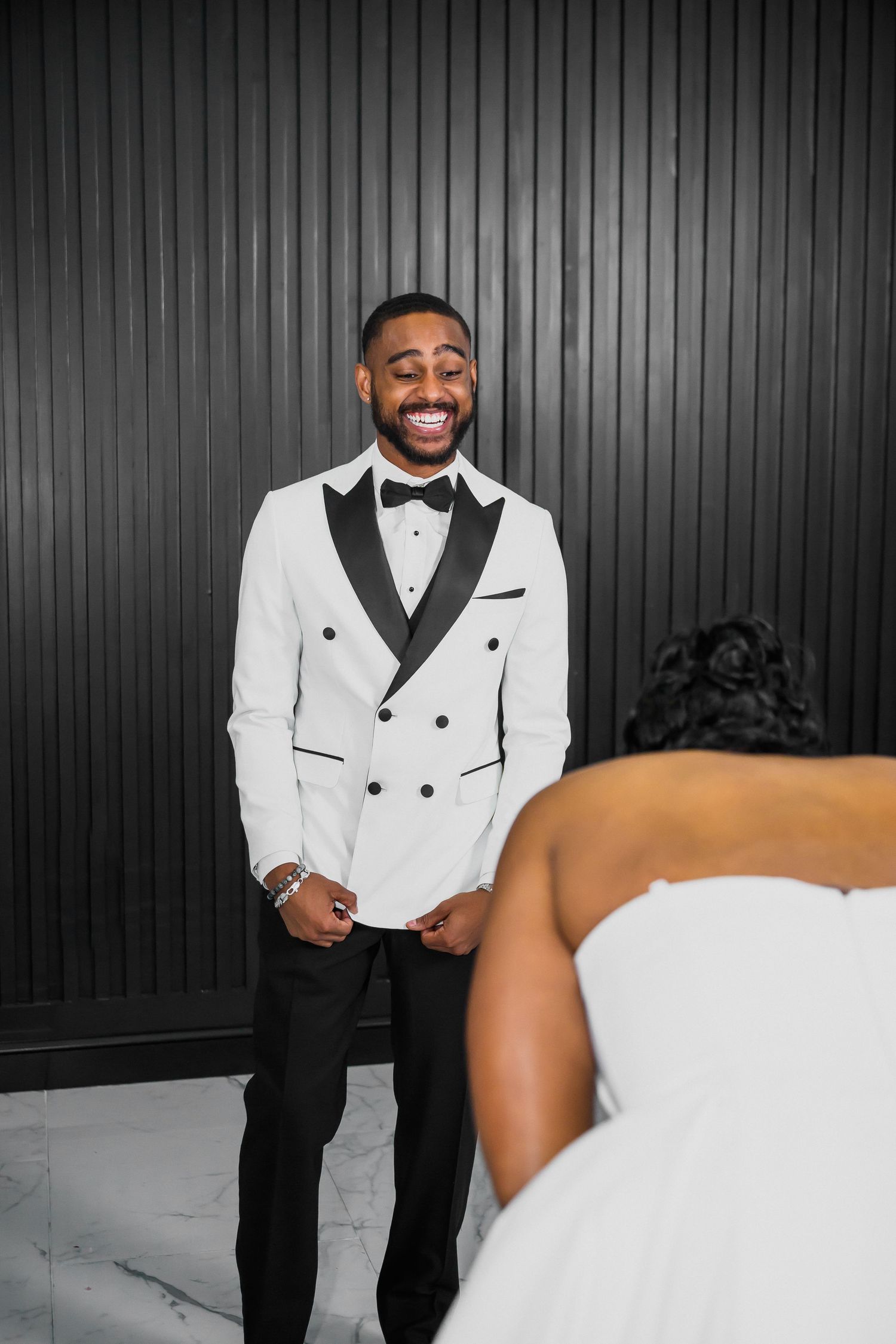 A person wearing a white tuxedo jacket and black bow tie poses against a dark background in a formal portrait series.