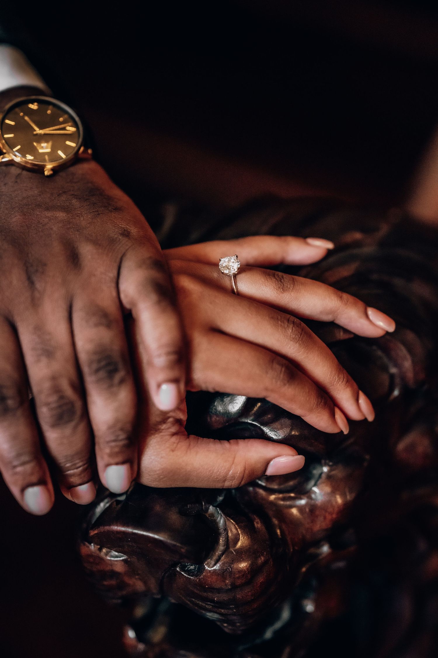 Close-up of hands with engagement ring in dramatic lighting.