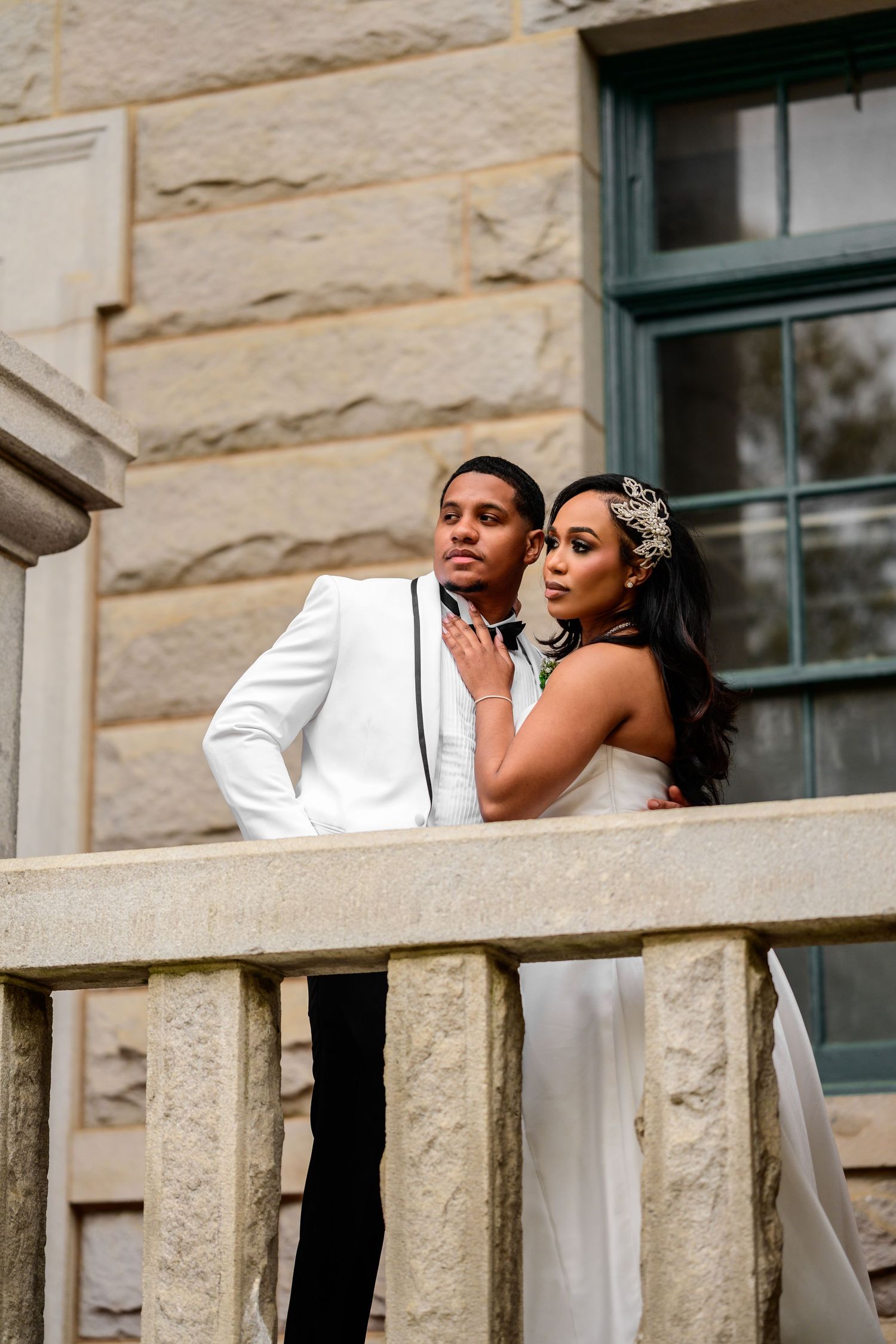 A wedding couple poses together against a stone building exterior.