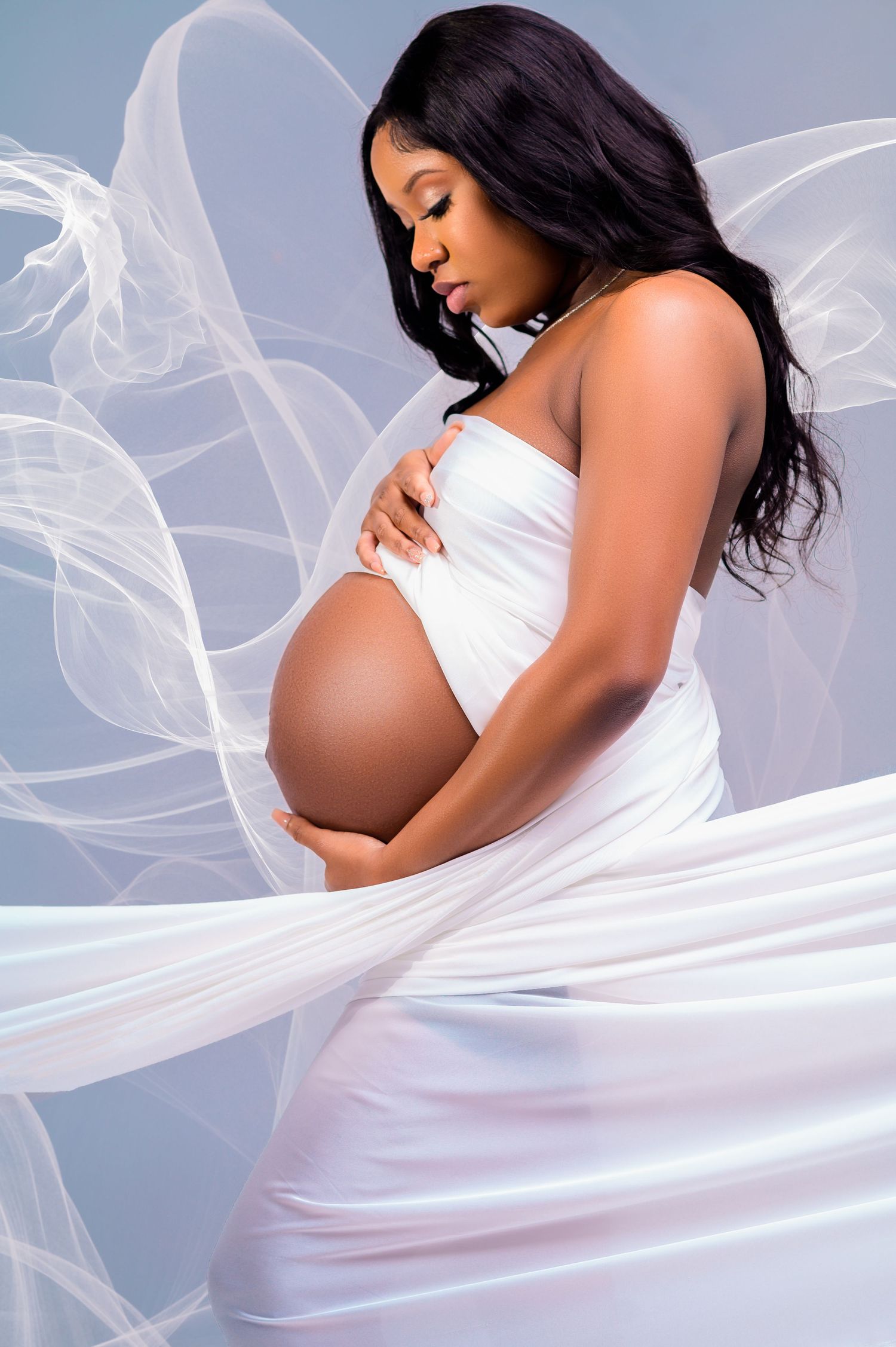 Elegant maternity photos featuring white flowing fabric and soft lighting.