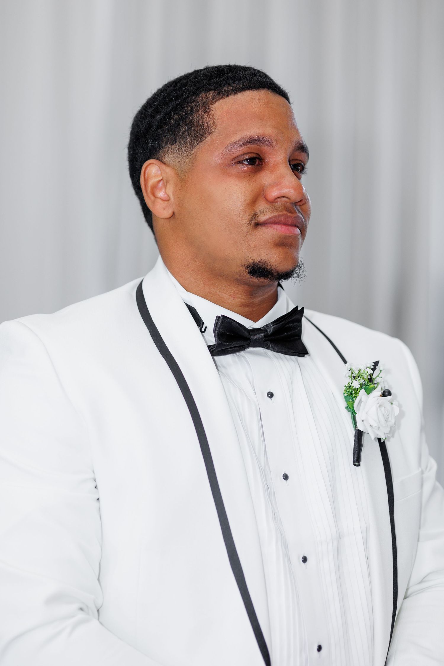 Groomsman in white tuxedo with black bow tie smiles during wedding portraits.