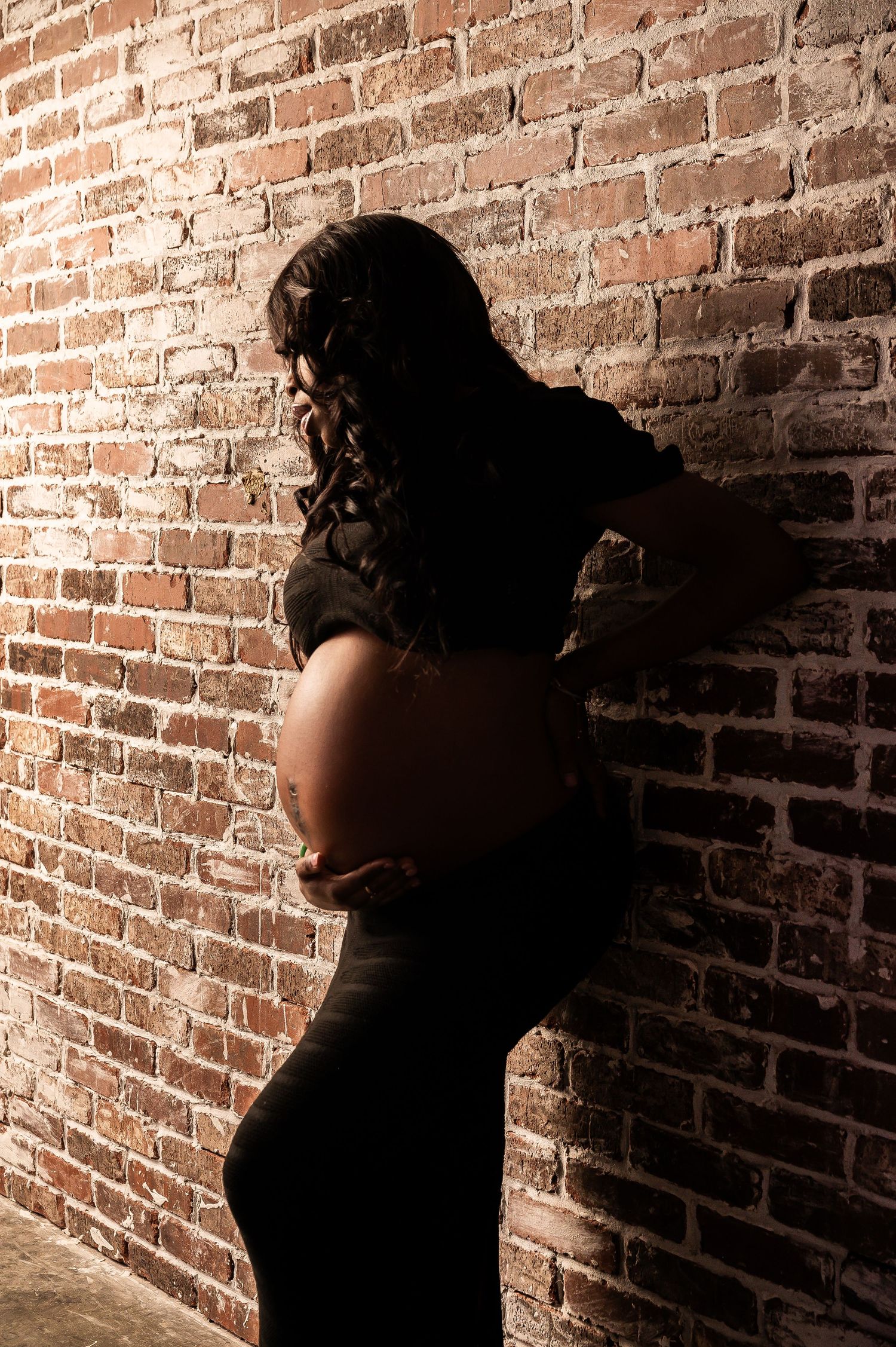 Artistic maternity silhouette against textured brick backdrop.