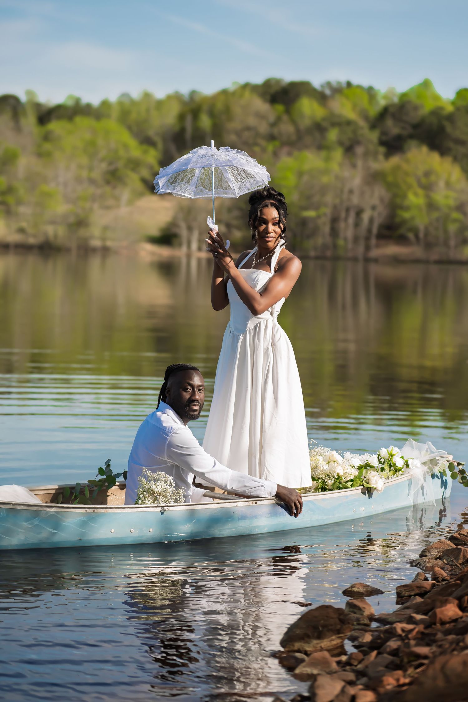 A romantic lakeside photo shoot with a white dress and clear umbrella creating dreamy reflections on the water.
