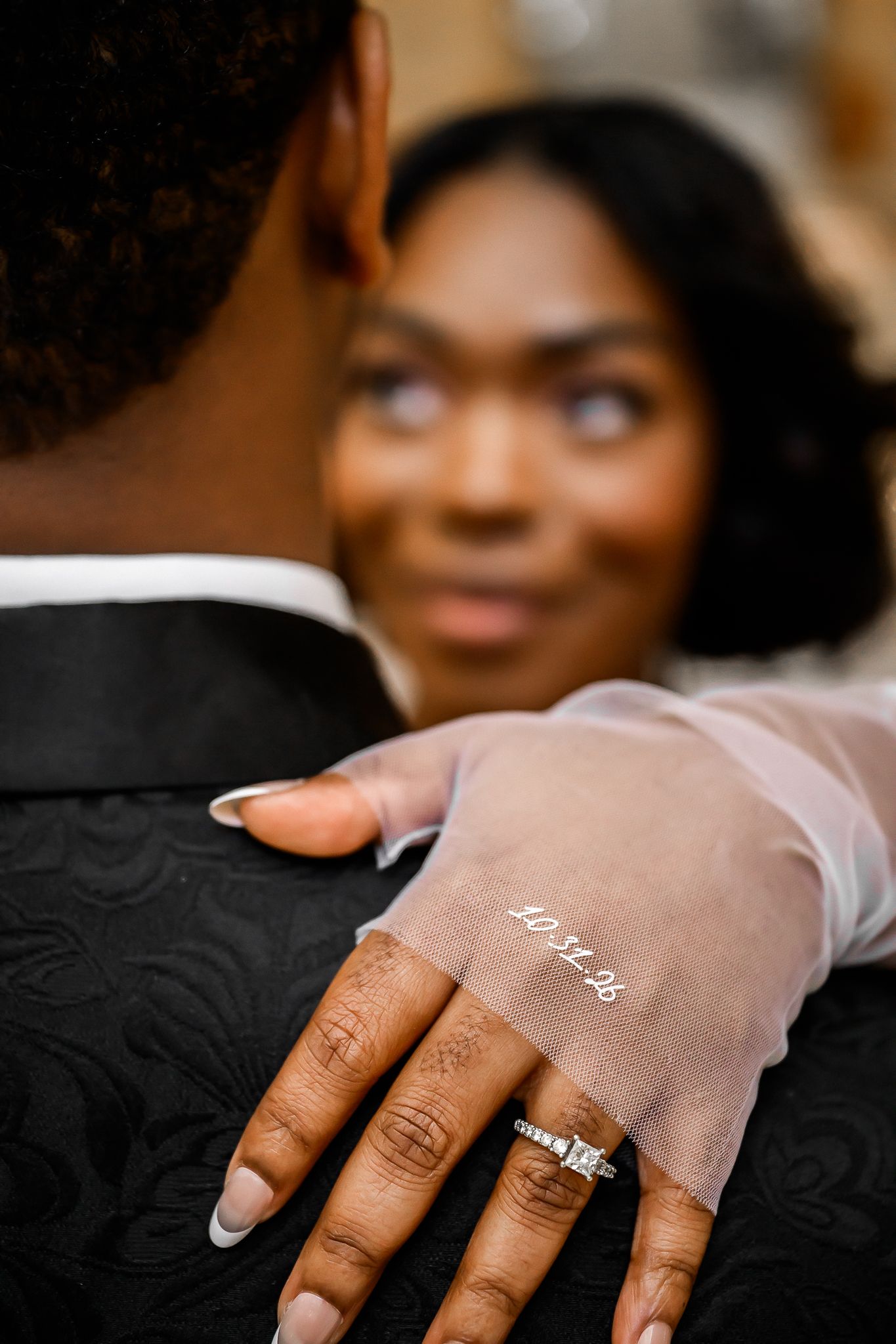 Close-up of engagement ring and sheer glove against formal black attire.