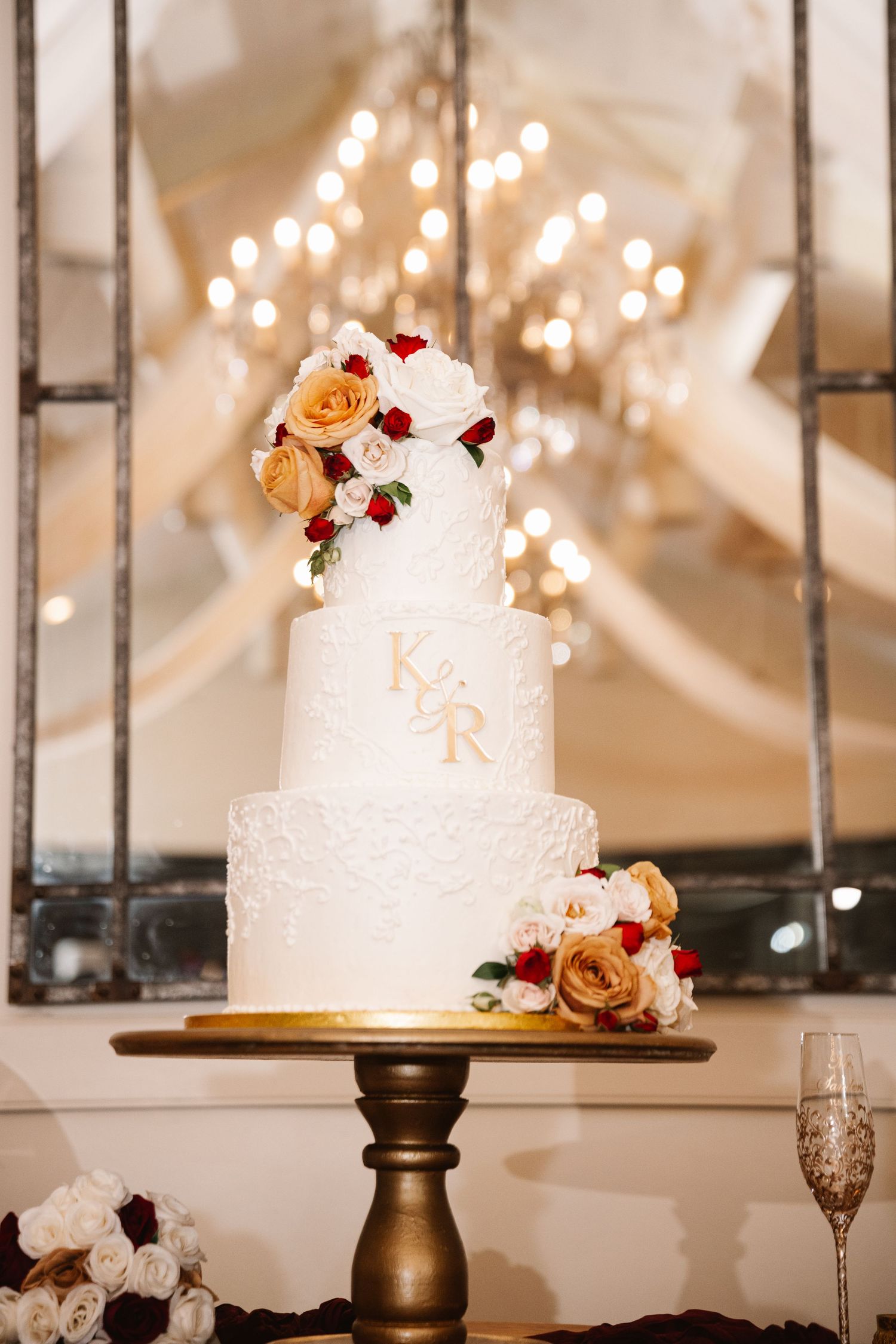 White wedding cakes decorated with burgundy and peach flowers displayed on gold stands.