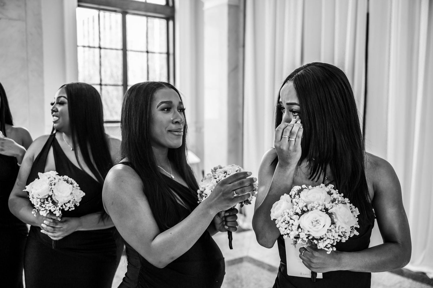Bridesmaids in black dresses holding white bouquets share joyful moments together.