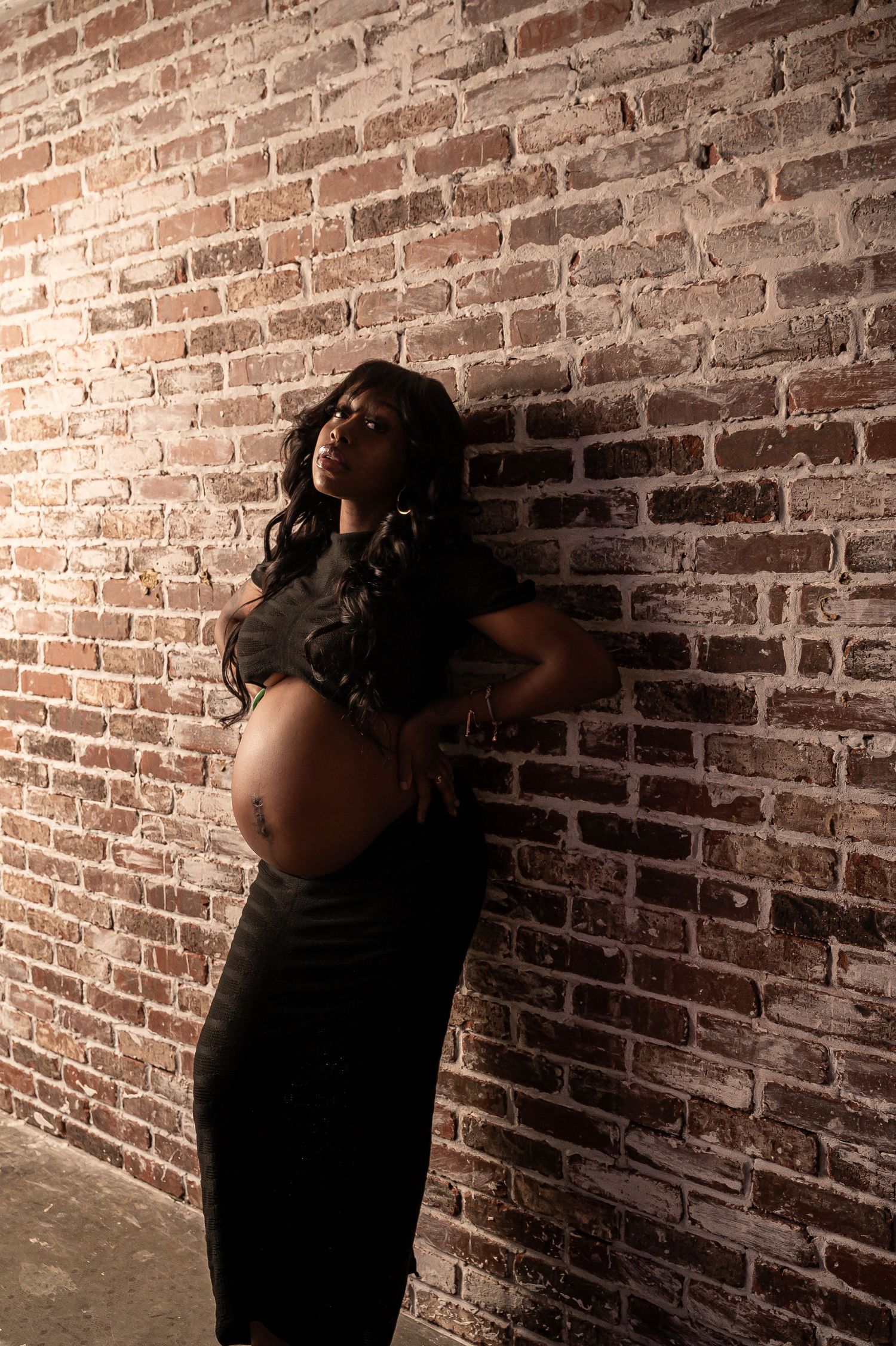 Dramatic maternity portrait against exposed brick wall.