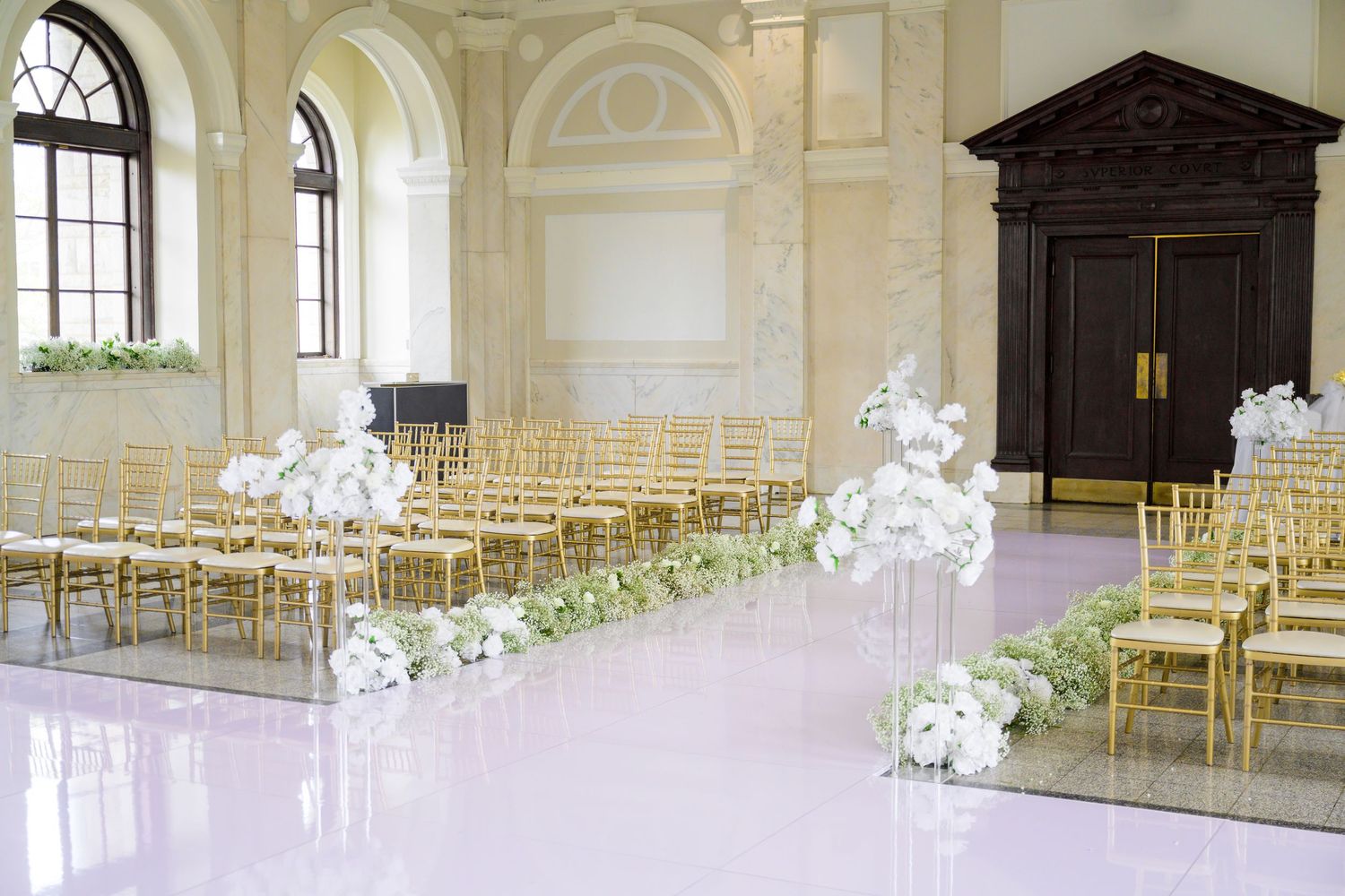 An elegant white wedding ceremony venue with gold chairs and floral decorations.