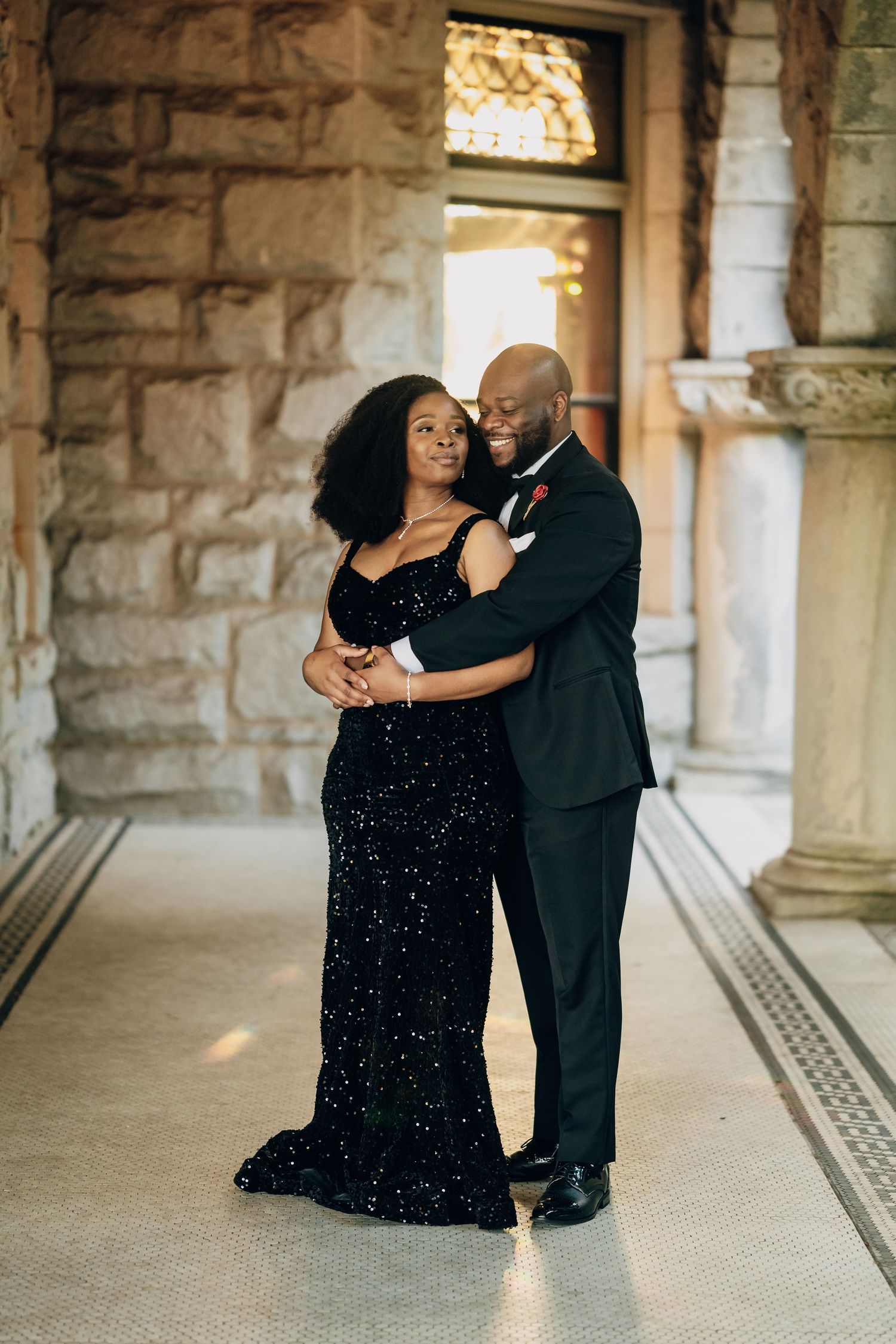 Couple dances together in formal wear under stone archway during photoshoot.