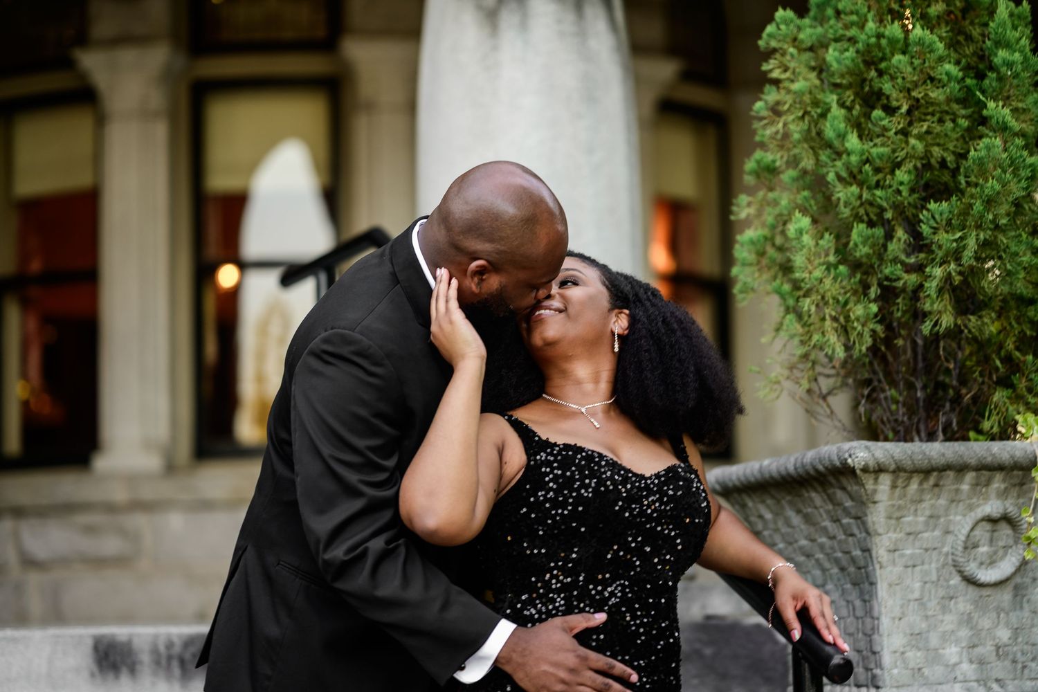 Joyful couple sharing intimate moment in formal wear by stone pillars.