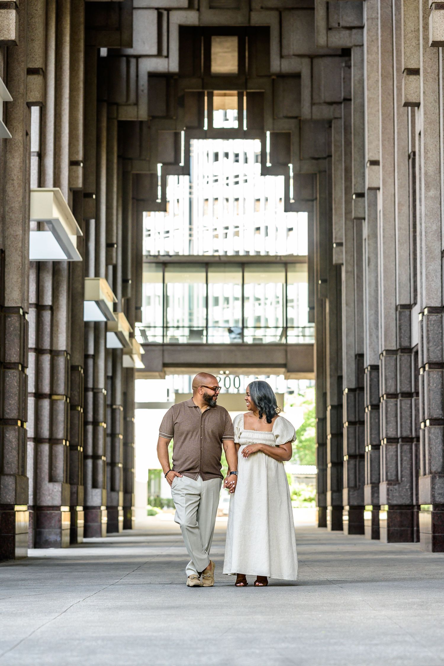 Couple walks through modern architectural space with geometric columns and natural lighting.
