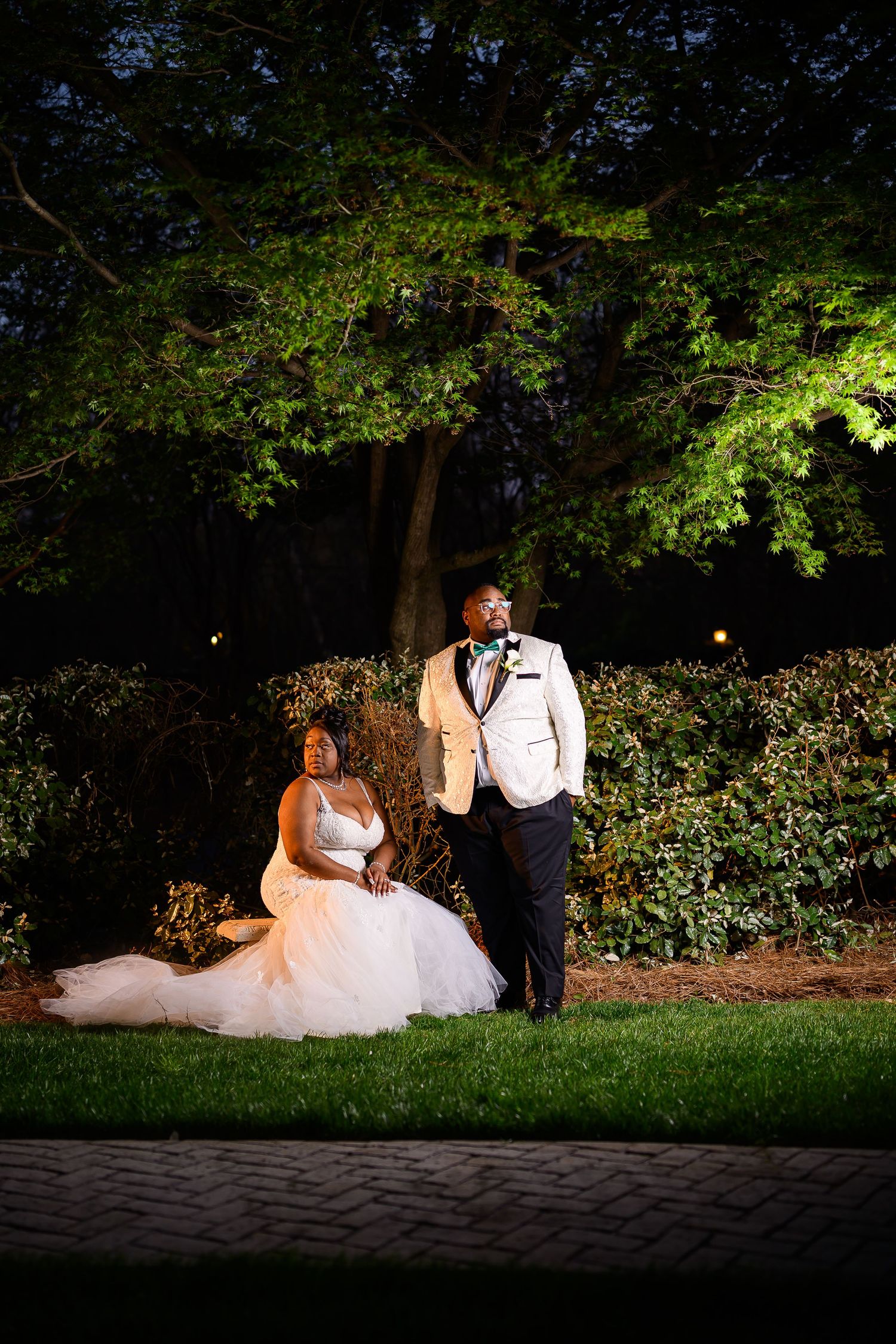 Evening garden wedding portrait with dramatic lighting highlighting trees and formal attire.