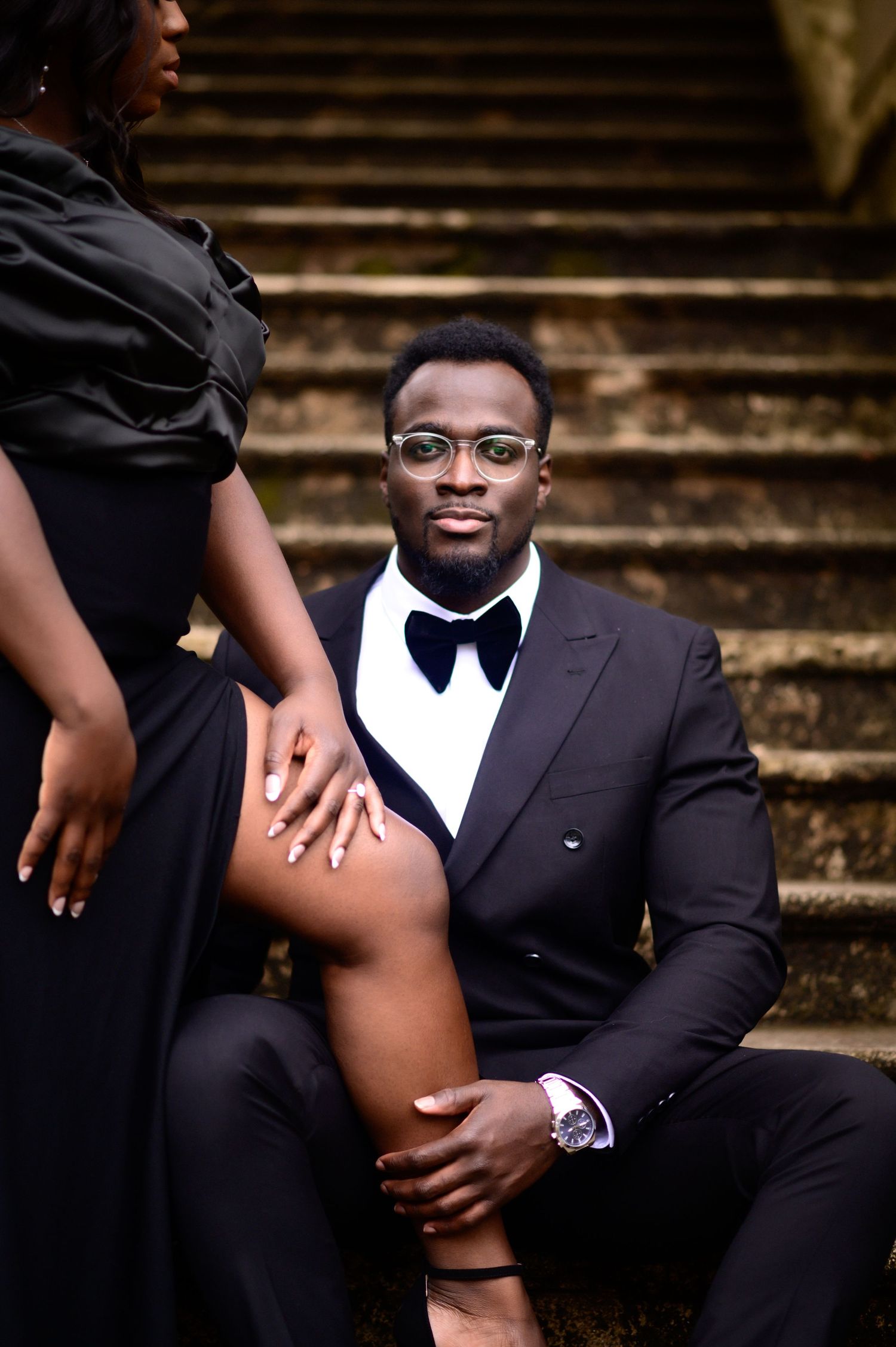 Elegant couple poses on stone steps in formal black attire for an intimate portrait session.