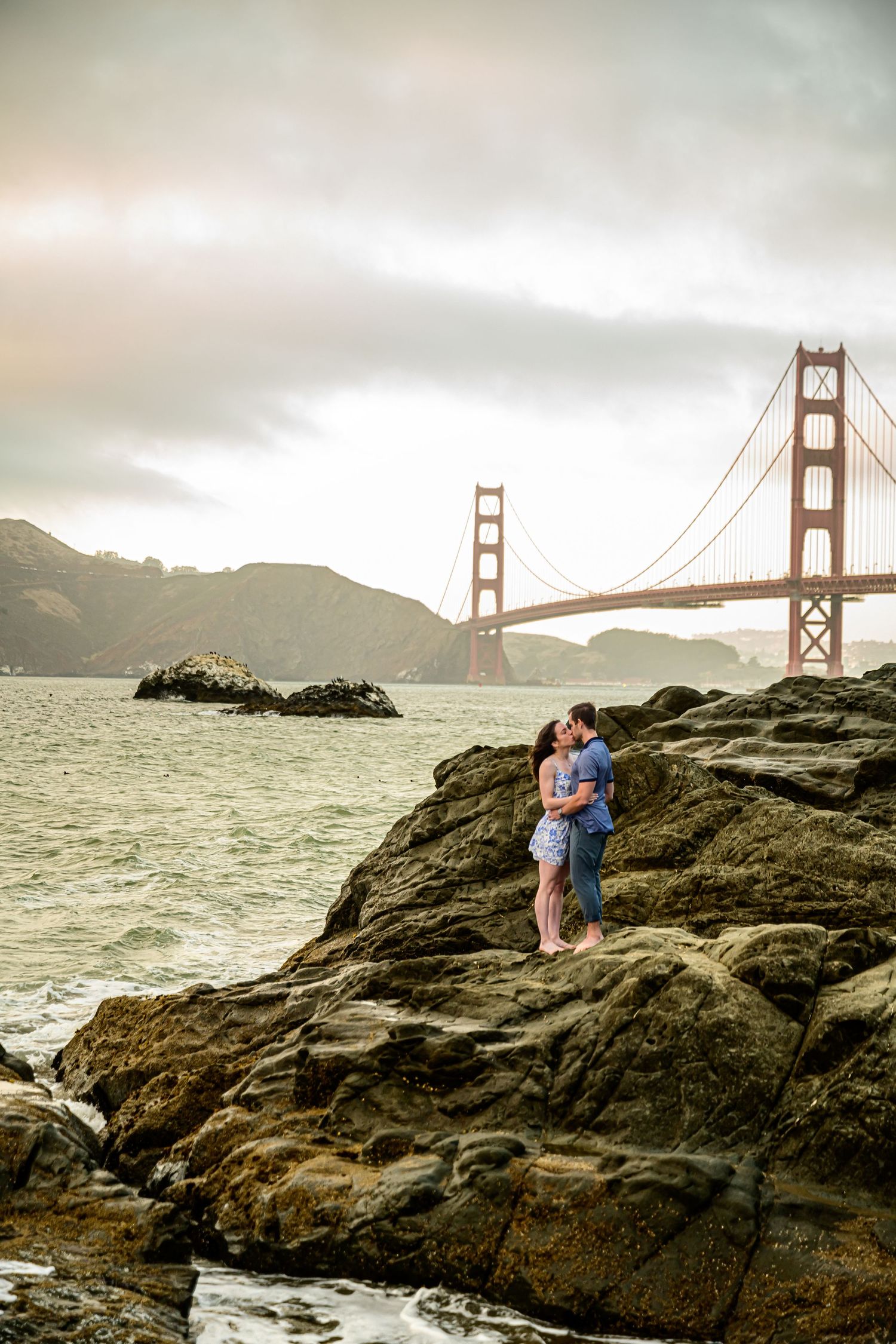 A romantic photoshoot on rocky shores with the Golden Gate Bridge creating a stunning backdrop.