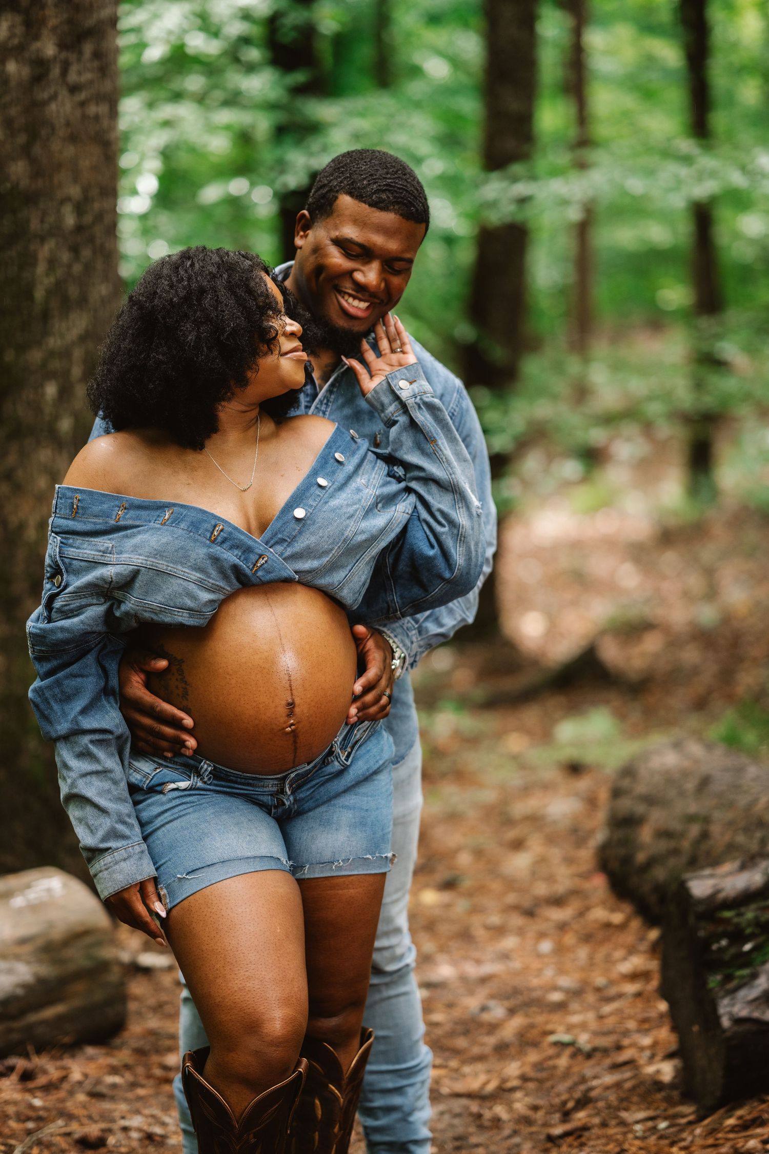 Maternity photoshoot in a forest setting with denim outfit and brown boots against natural woodland backdrop.