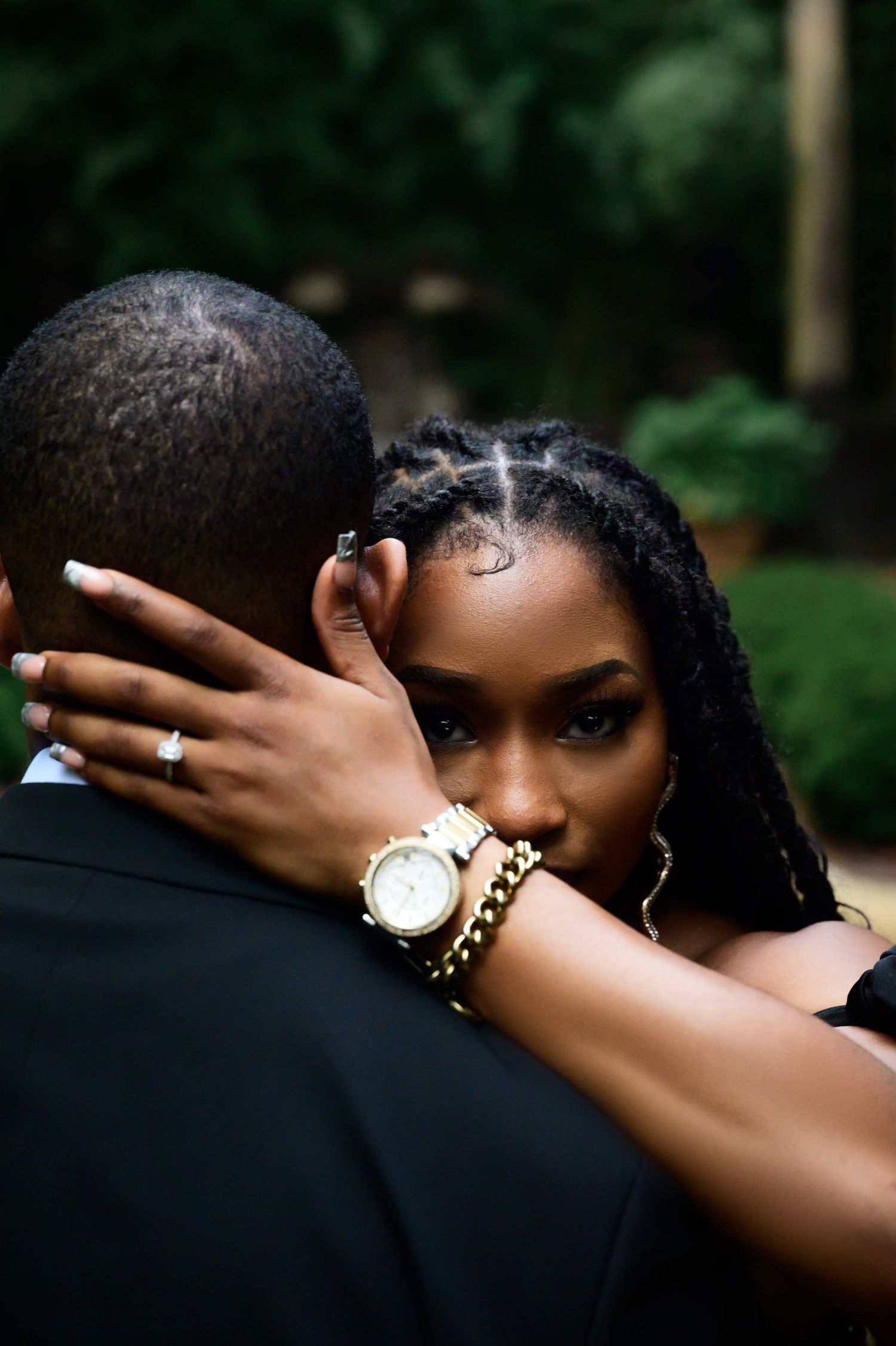 Intimate engagement photo showing couple embracing with gold jewelry and watch details visible.