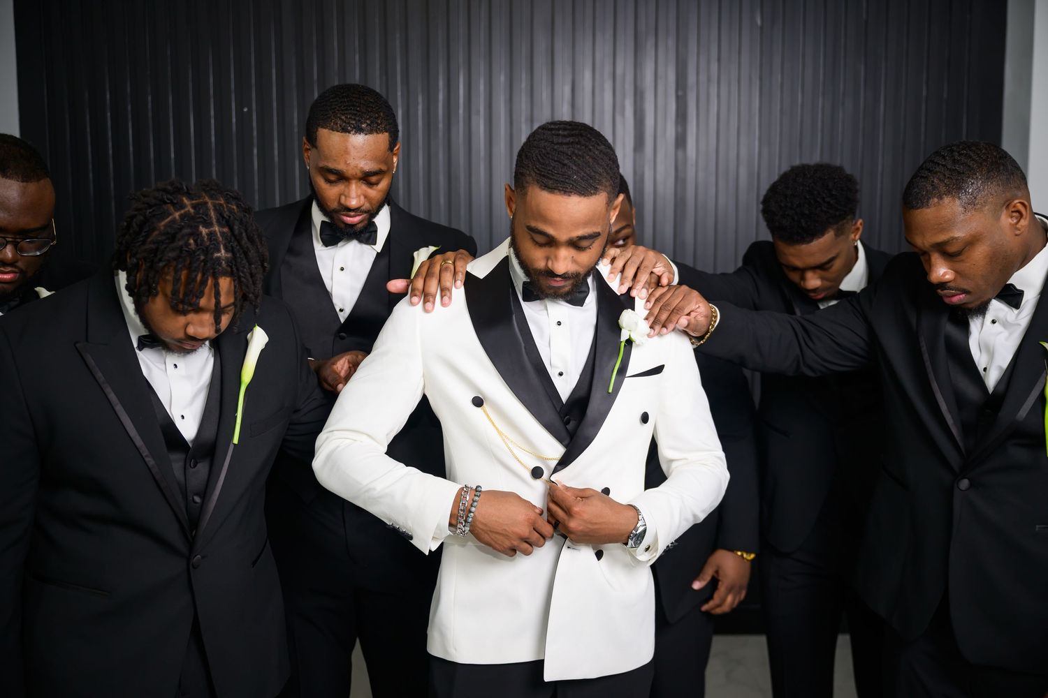 A group of men in formal black and white tuxedos pose together for a wedding party photo.