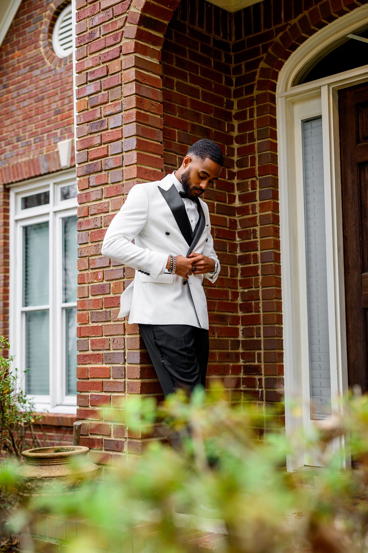 A person in a white dress shirt and black vest stands near a brick building entrance with arched windows.