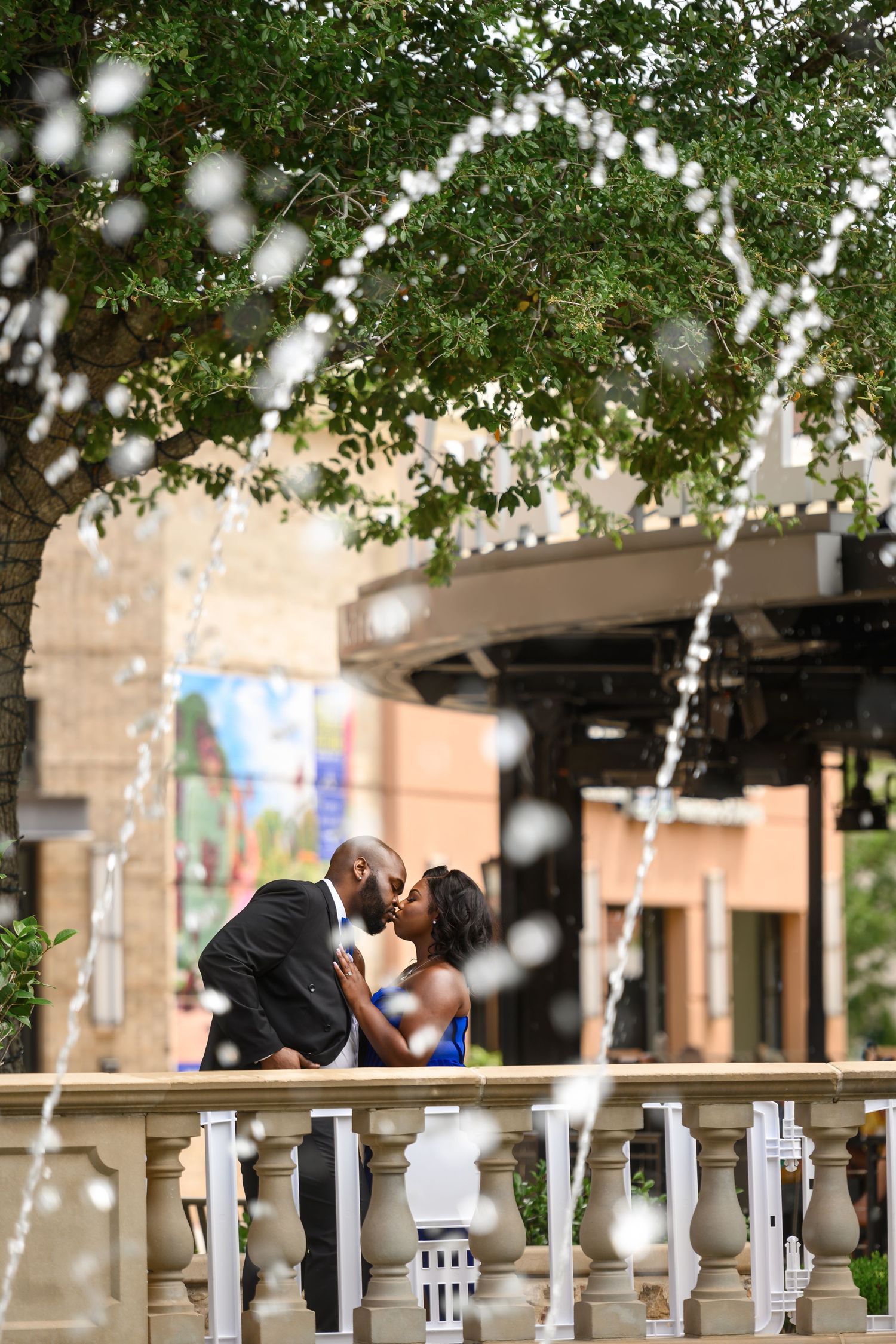 Couple shares tender moment under string lights and white balustrade outdoors.