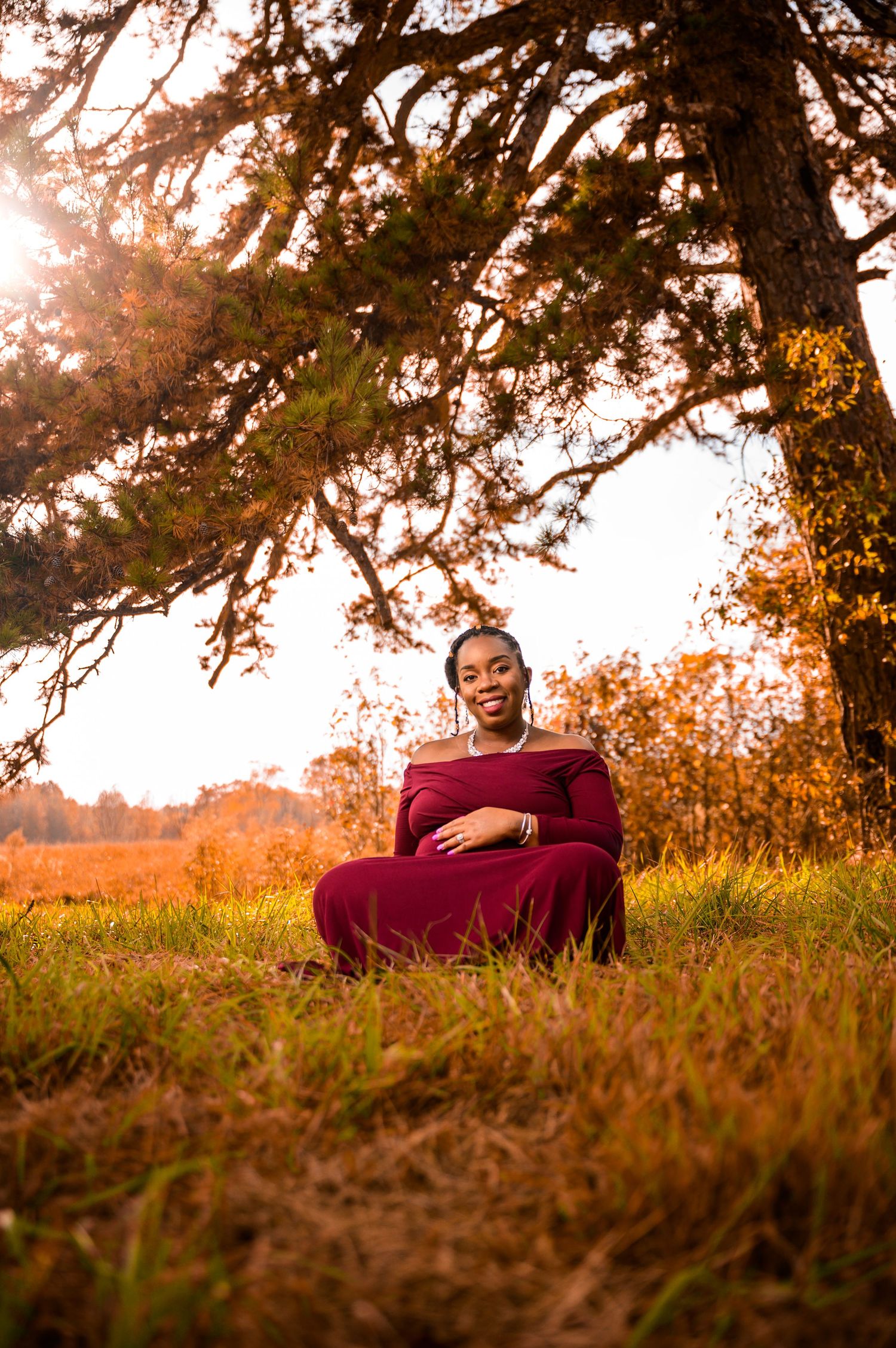 Autumn maternity session with warm sunlight filtering through trees.
