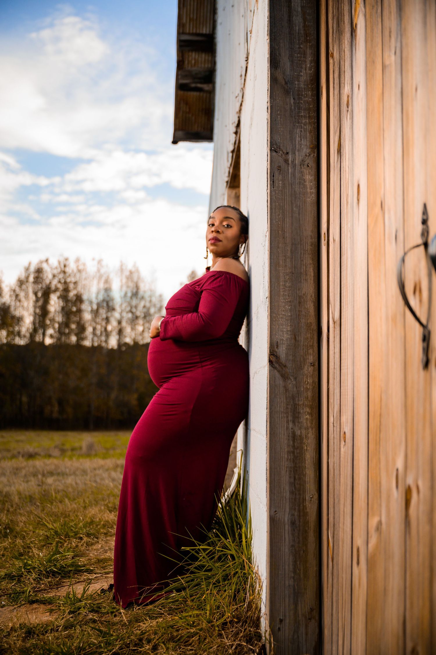 Maternity photos taken against rustic wooden pillars during golden hour.