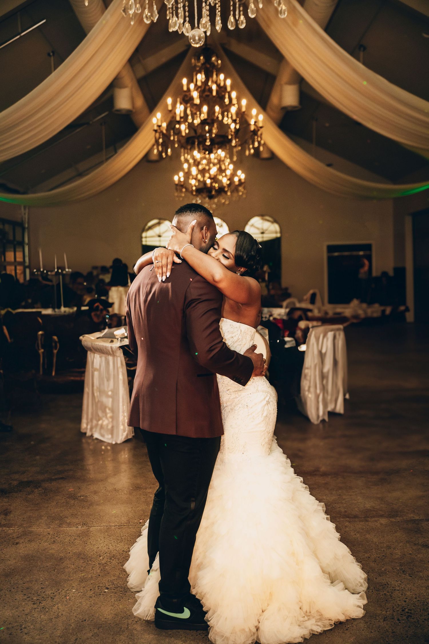 Couple sharing a romantic dance in an elegant ballroom decorated with white drapes and crystal chandeliers.