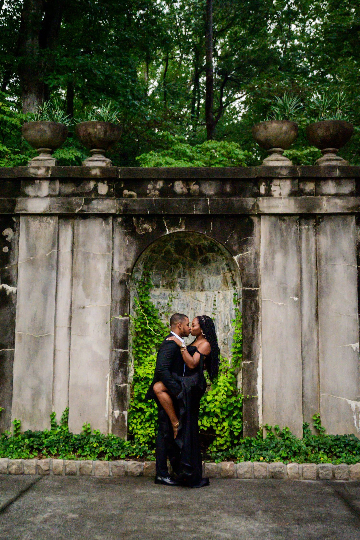 Couple sharing intimate moment in front of ivy-covered stone garden archway.