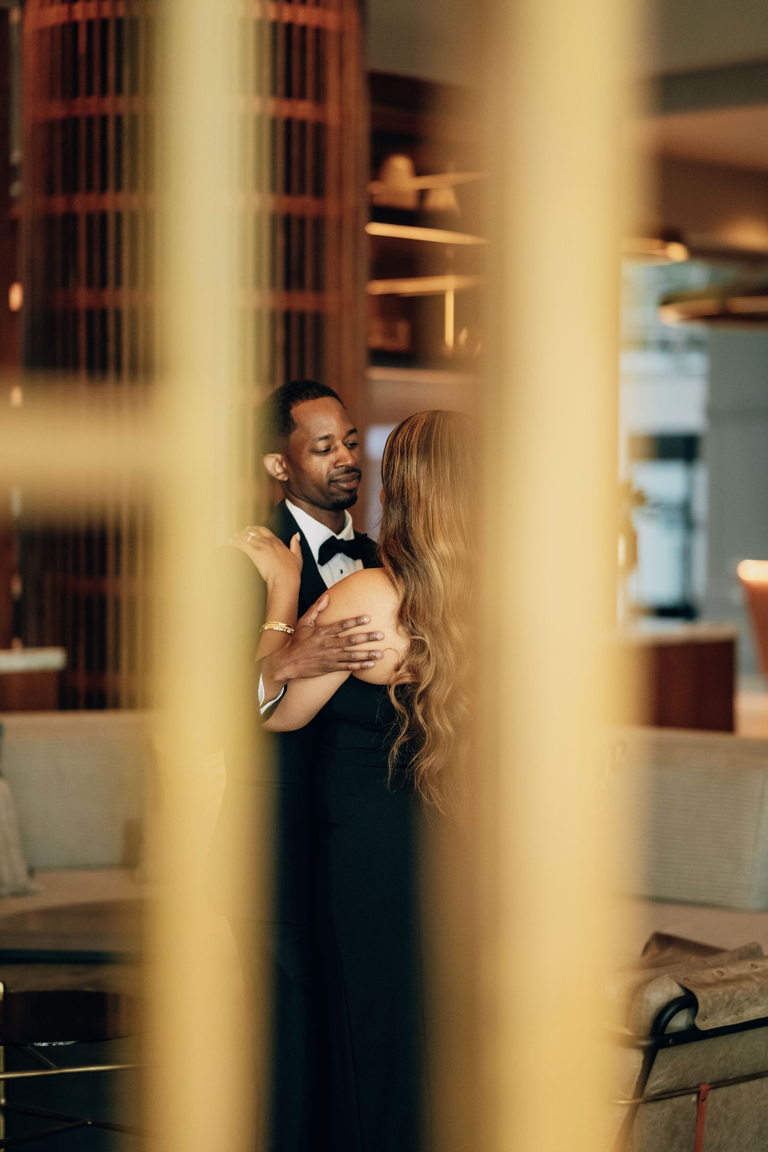 Artistic portrait through golden columns in dimly lit elegant interior setting.