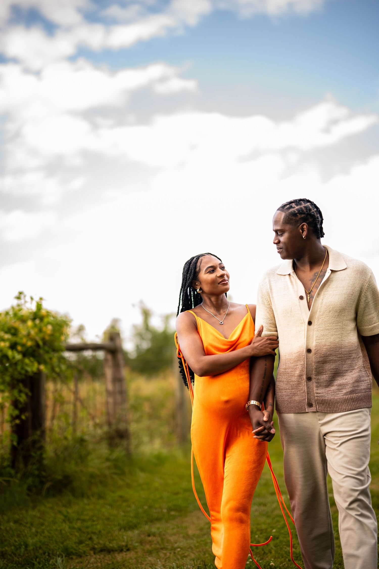 A couple shares a joyful moment together in a sunny field with blue skies overhead.