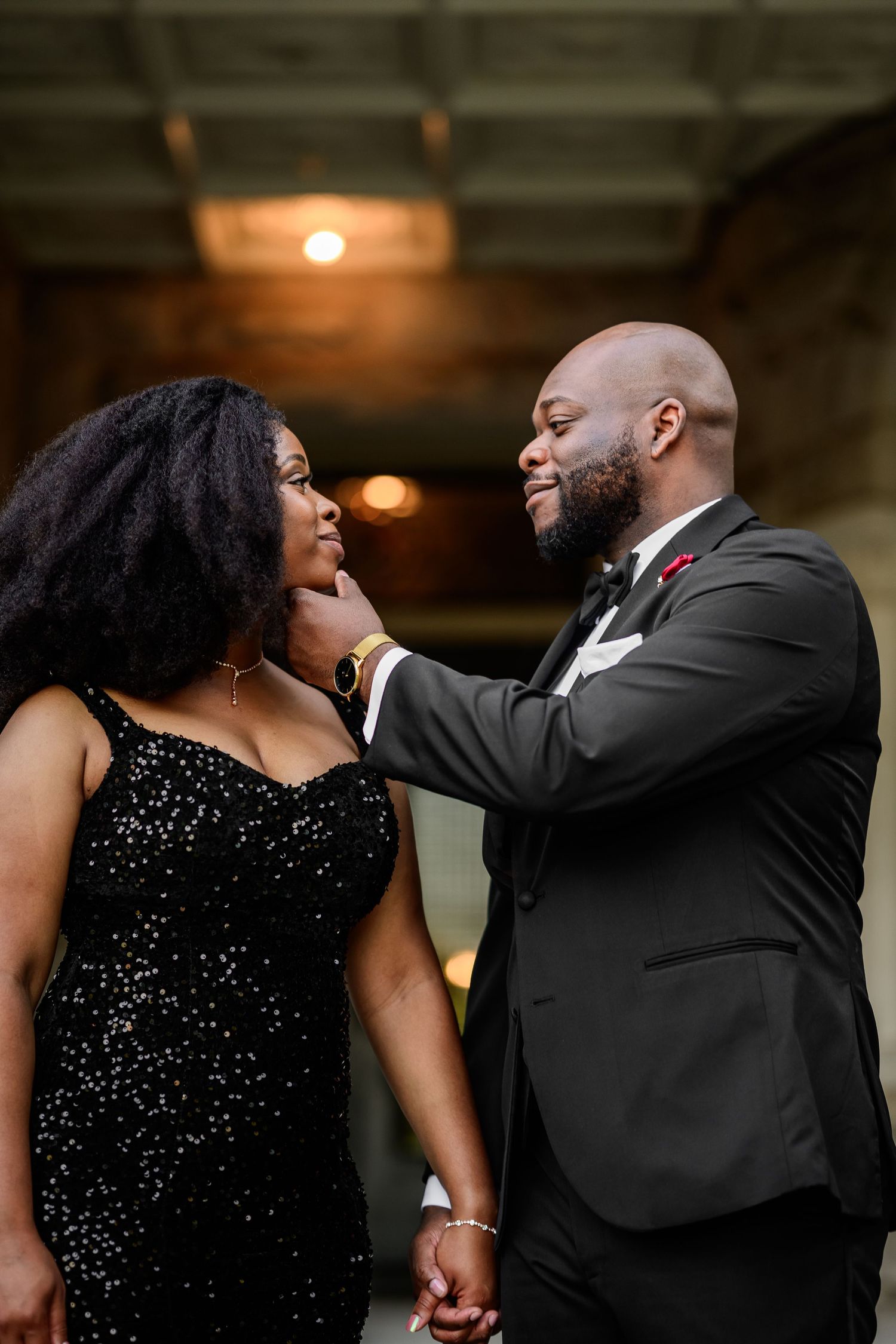Couple shares tender moments in formal attire against stone building backdrop.