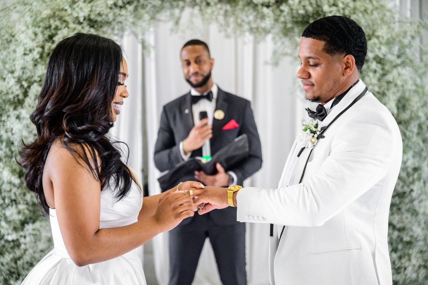 Elegant wedding ceremony with white drapery and floral arch decorations in a bright indoor space.