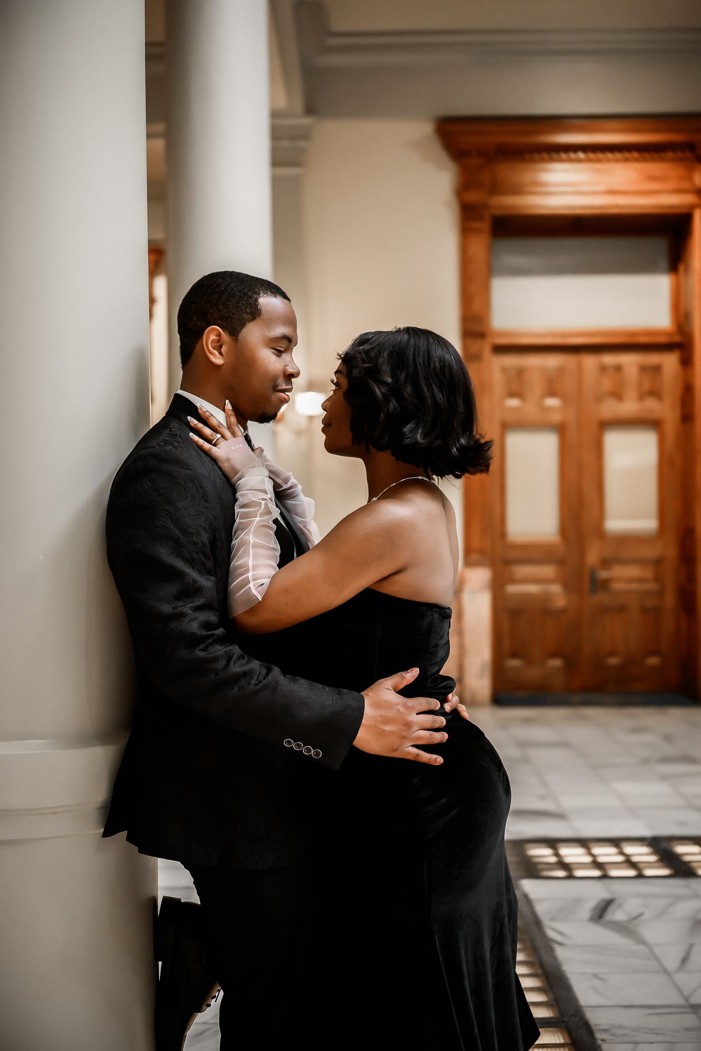 Intimate moment between couple in formal wear against white column and wooden door.