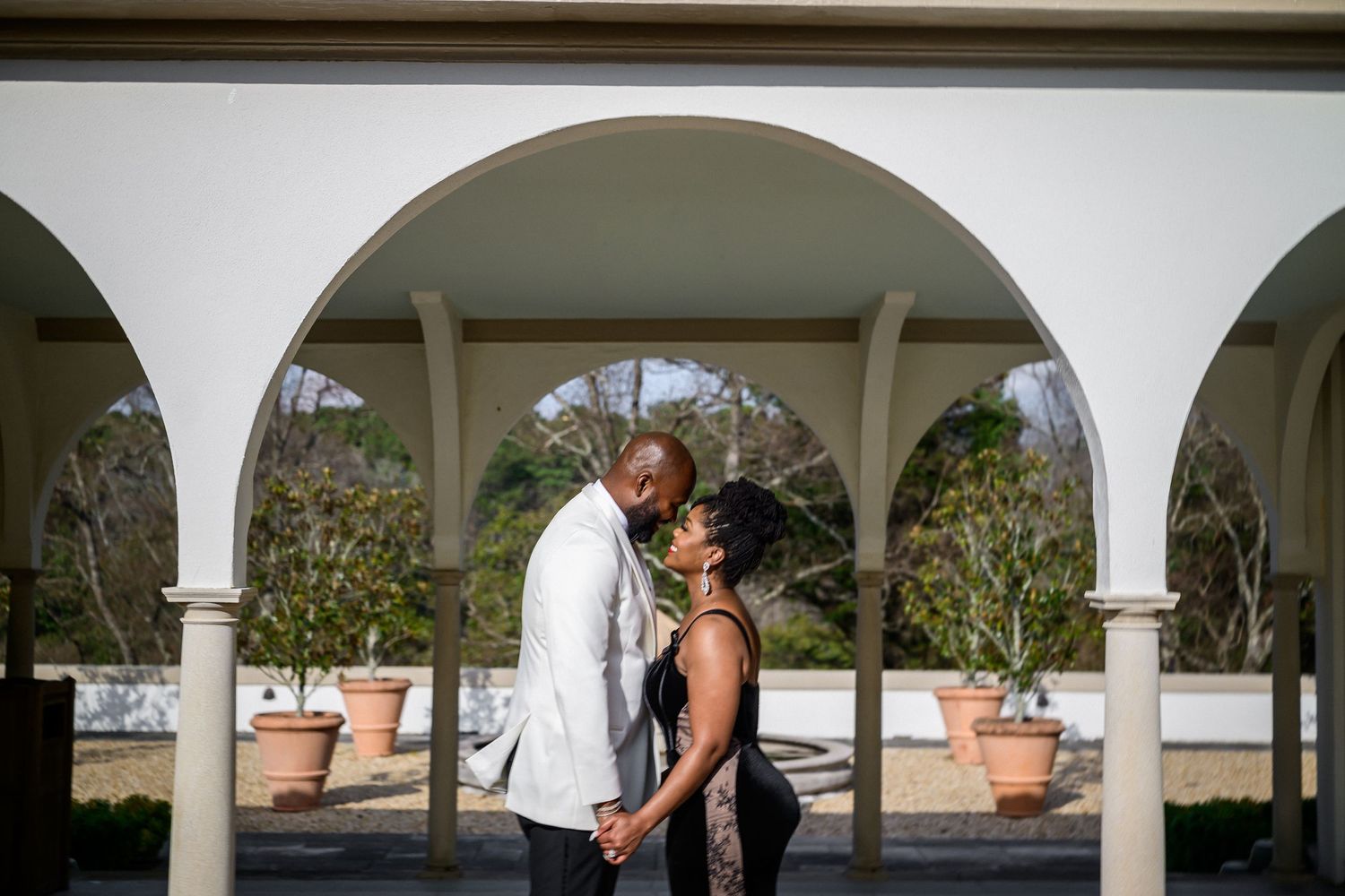 A couple shares a romantic moment under white arched columns in an elegant outdoor setting during a wedding ceremony.