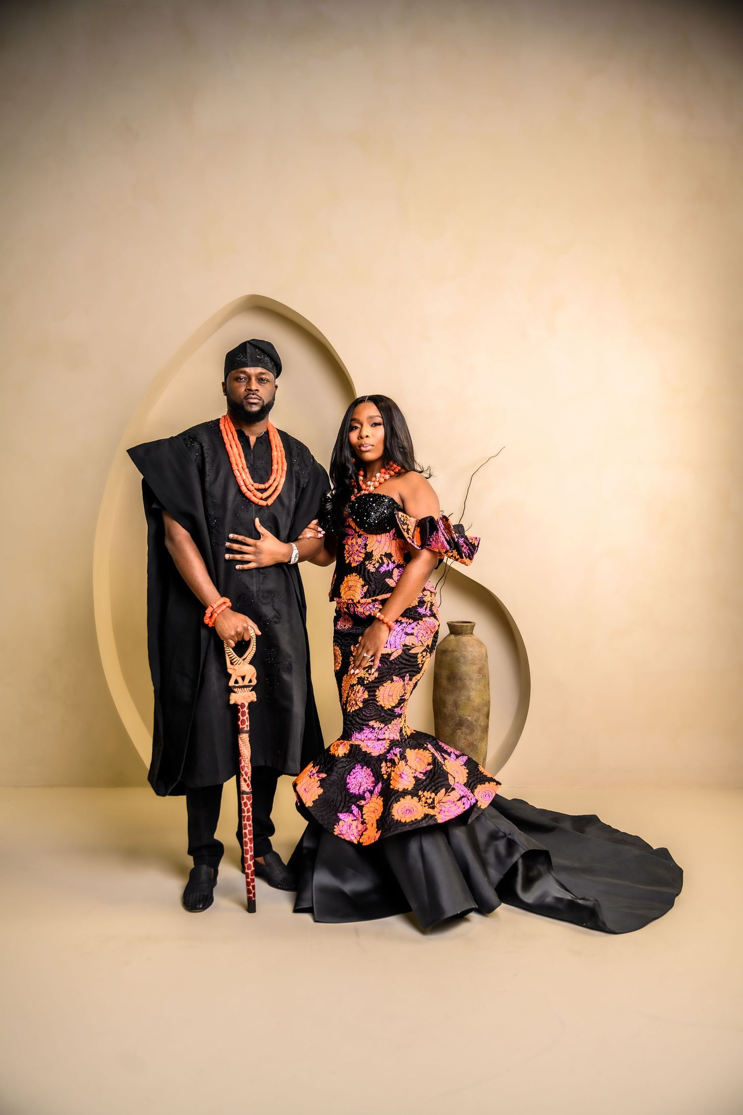 Studio portrait session with couple in formal attire against cream backdrop with architectural elements.