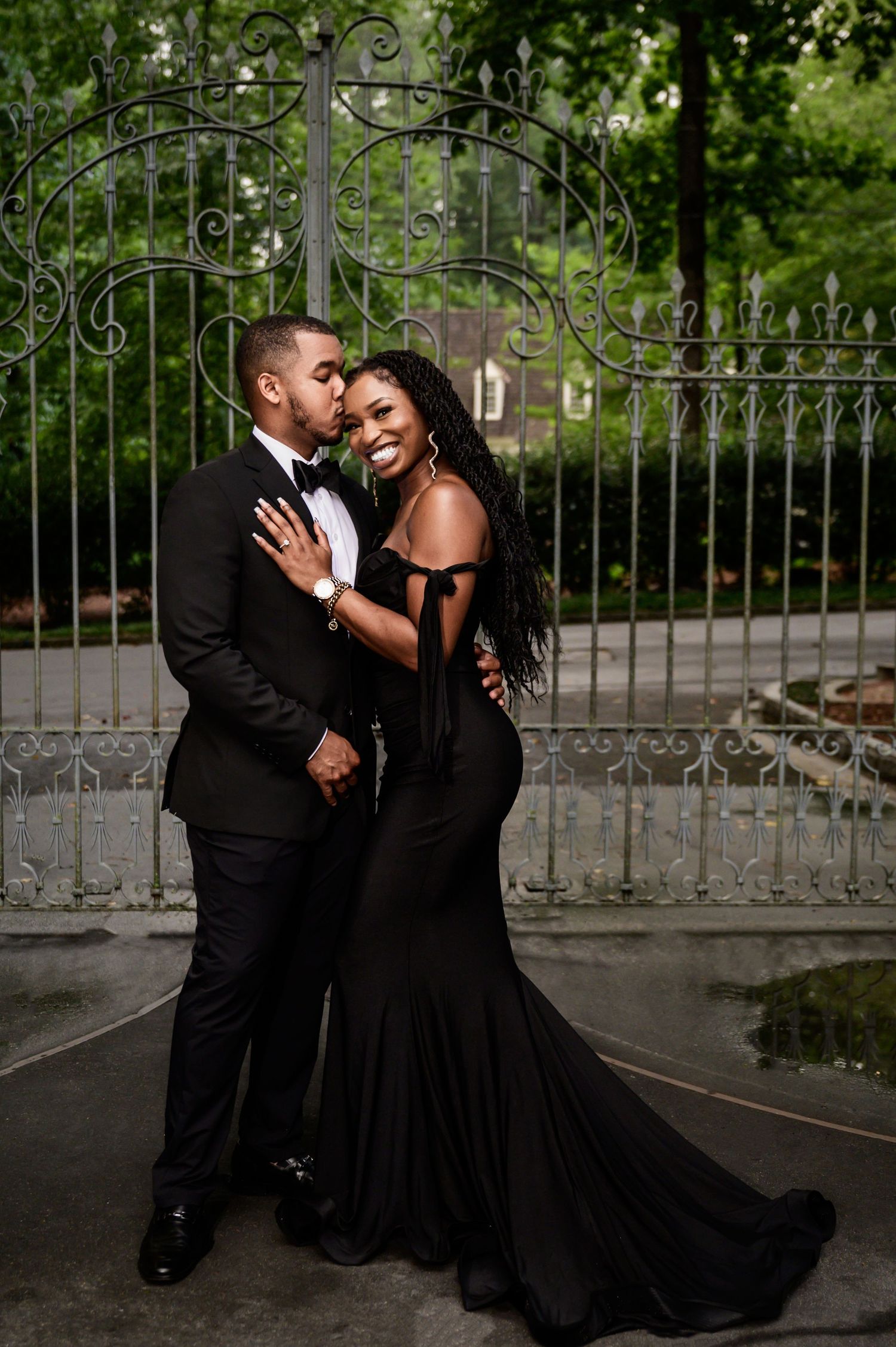 Romantic couple in formal black attire share intimate moments against an ornate iron gate backdrop.
