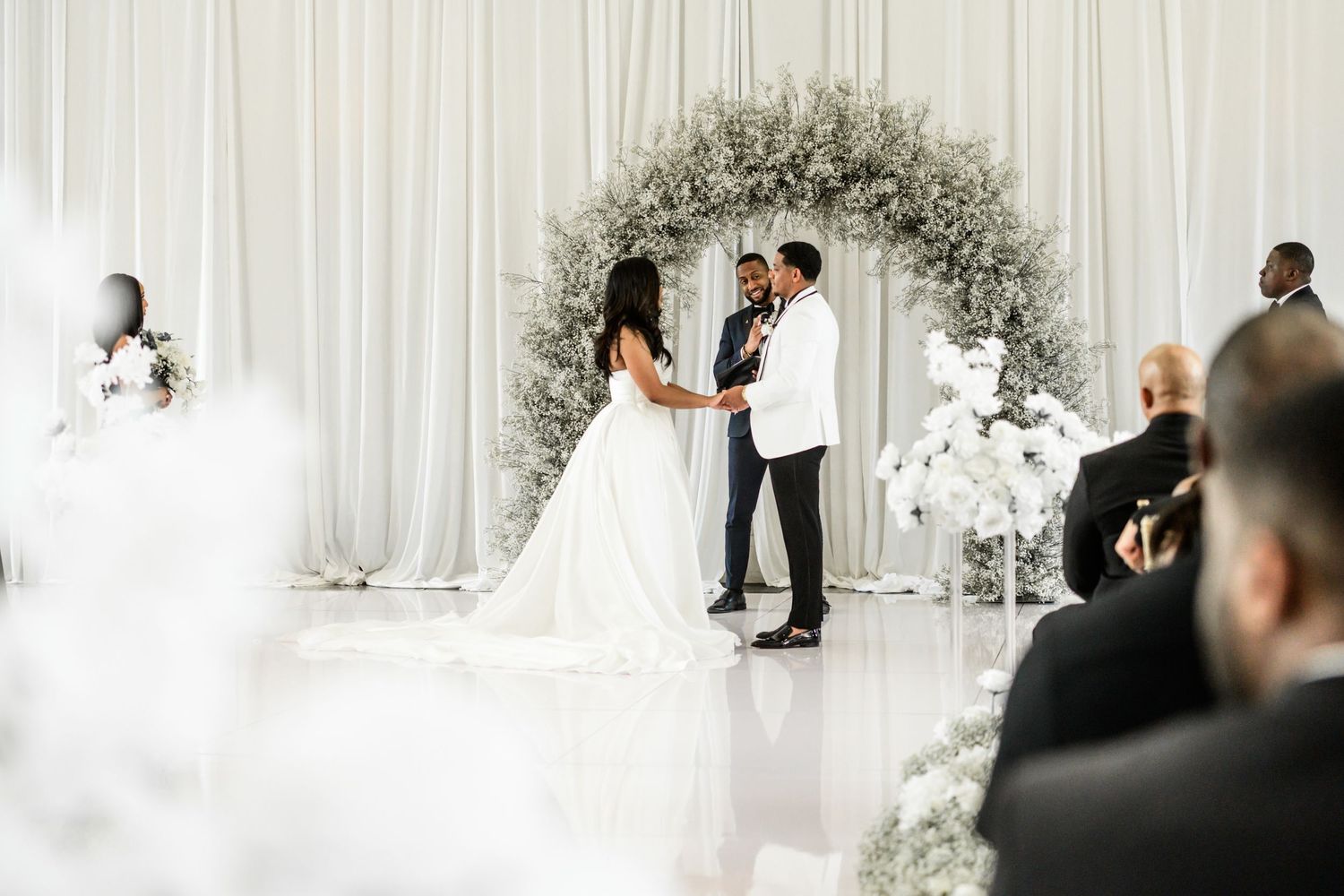 Wedding ceremony setup with white draping and floral arch in an elegant indoor venue.
