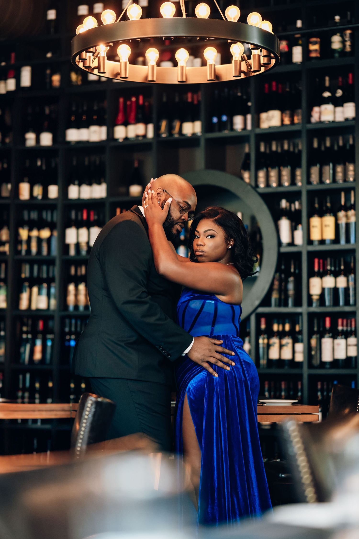 Couple in formal attire shares romantic moment in wine cellar with ambient lighting.