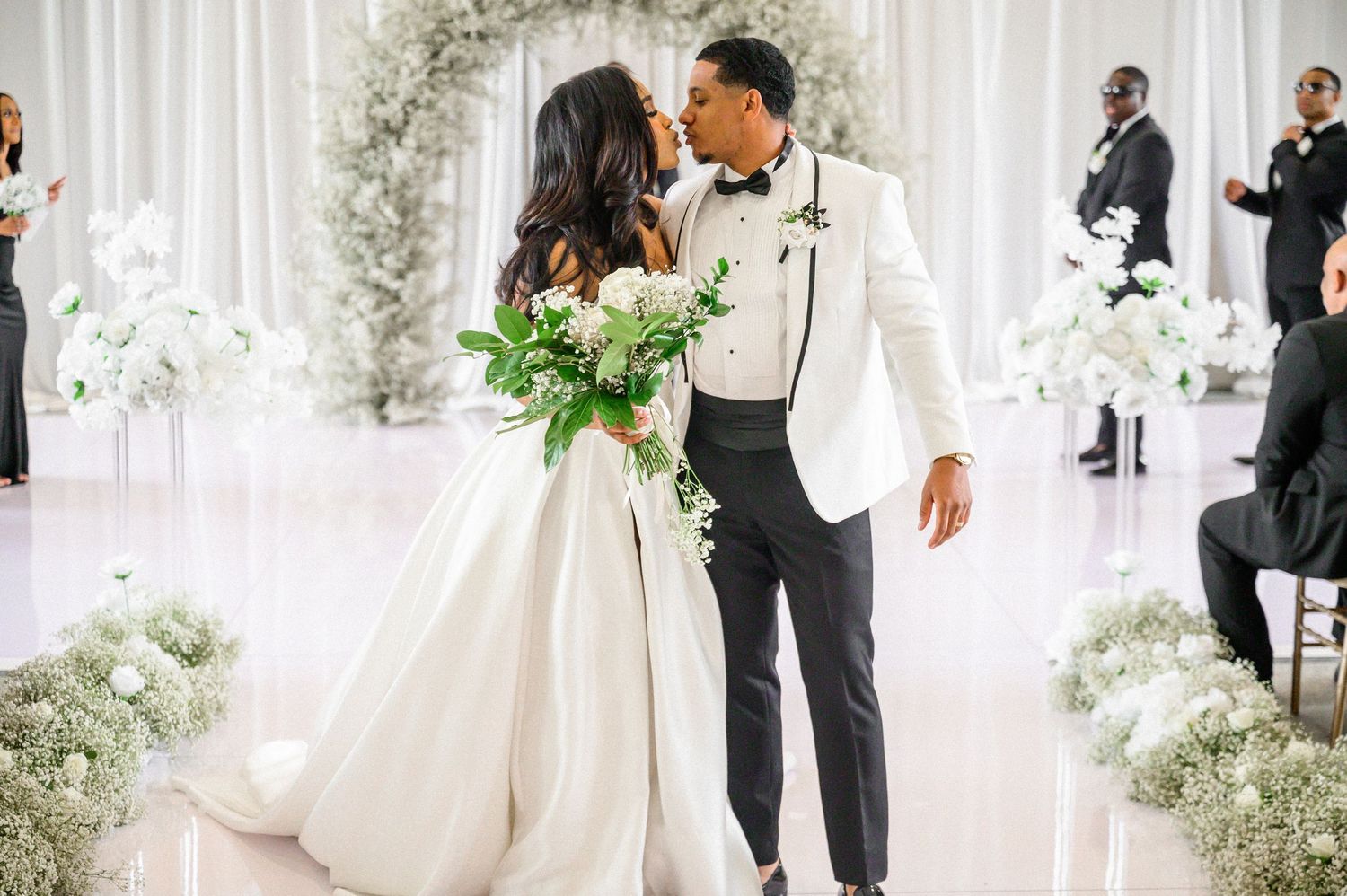 Wedding ceremony moments captured in an elegant white room with floral decorations.