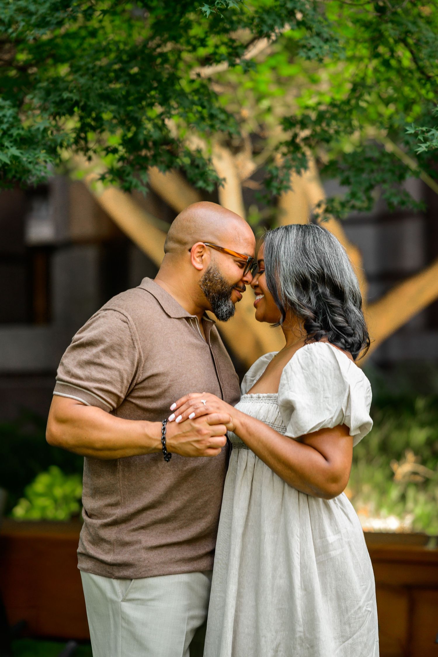 Couple dancing and embracing in a garden setting with lush greenery.